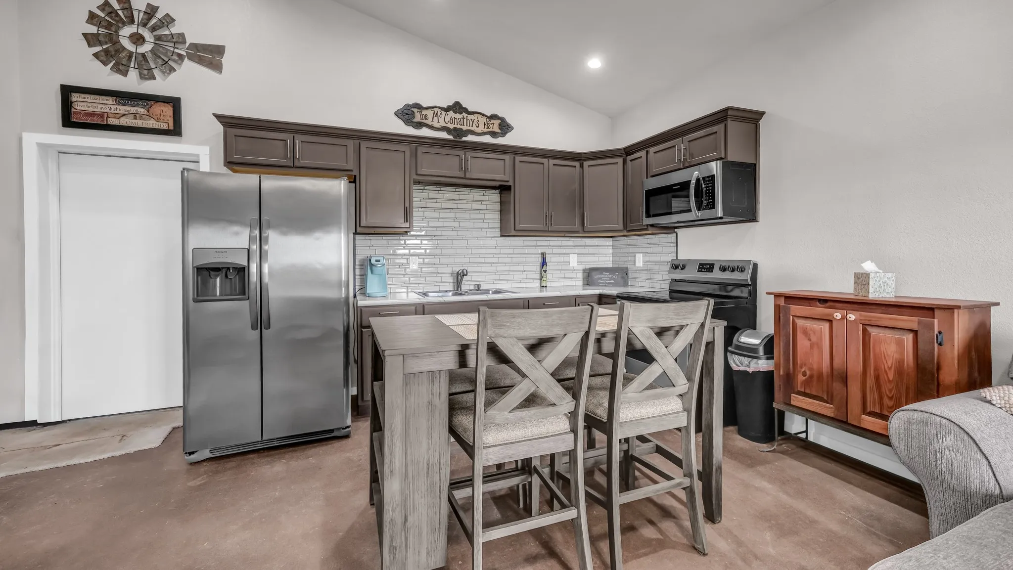 Kitchen featuring appliances with stainless steel finishes, tasteful backsplash, concrete floors, dark brown cabinets, and high vaulted ceiling