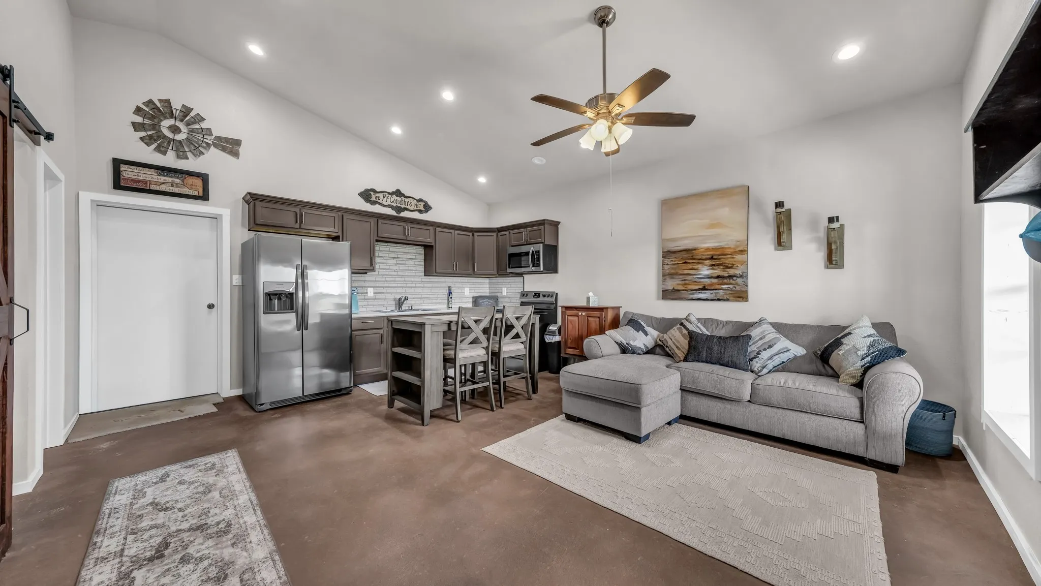 Living area with a barn door, recessed lighting, ceiling fan, high vaulted ceiling, and concrete floors