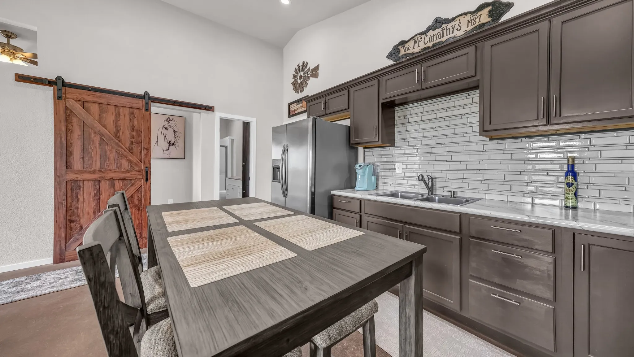 Kitchen with decorative backsplash, stainless steel refrigerator with ice dispenser, a barn door, dark brown cabinets, and finished concrete floors