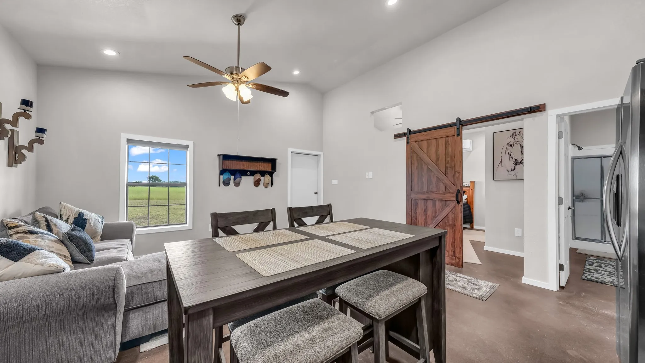Dining room with finished concrete floors, a barn door, high vaulted ceiling, a ceiling fan, and recessed lighting