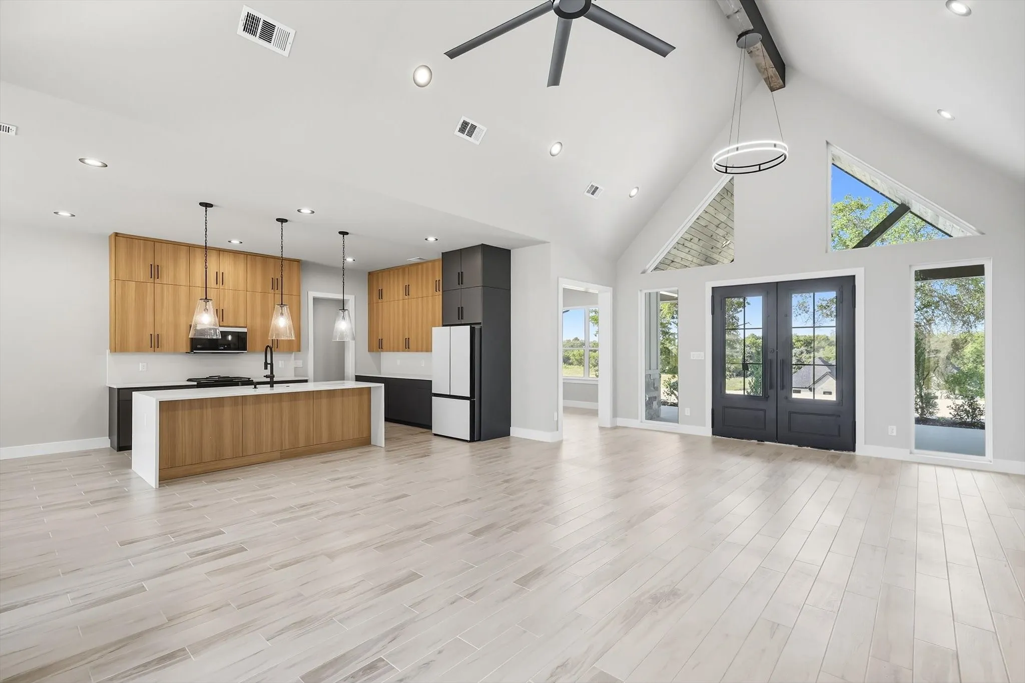 Kitchen featuring decorative light fixtures, open floor plan, high vaulted ceiling, beam ceiling, and an island with sink
