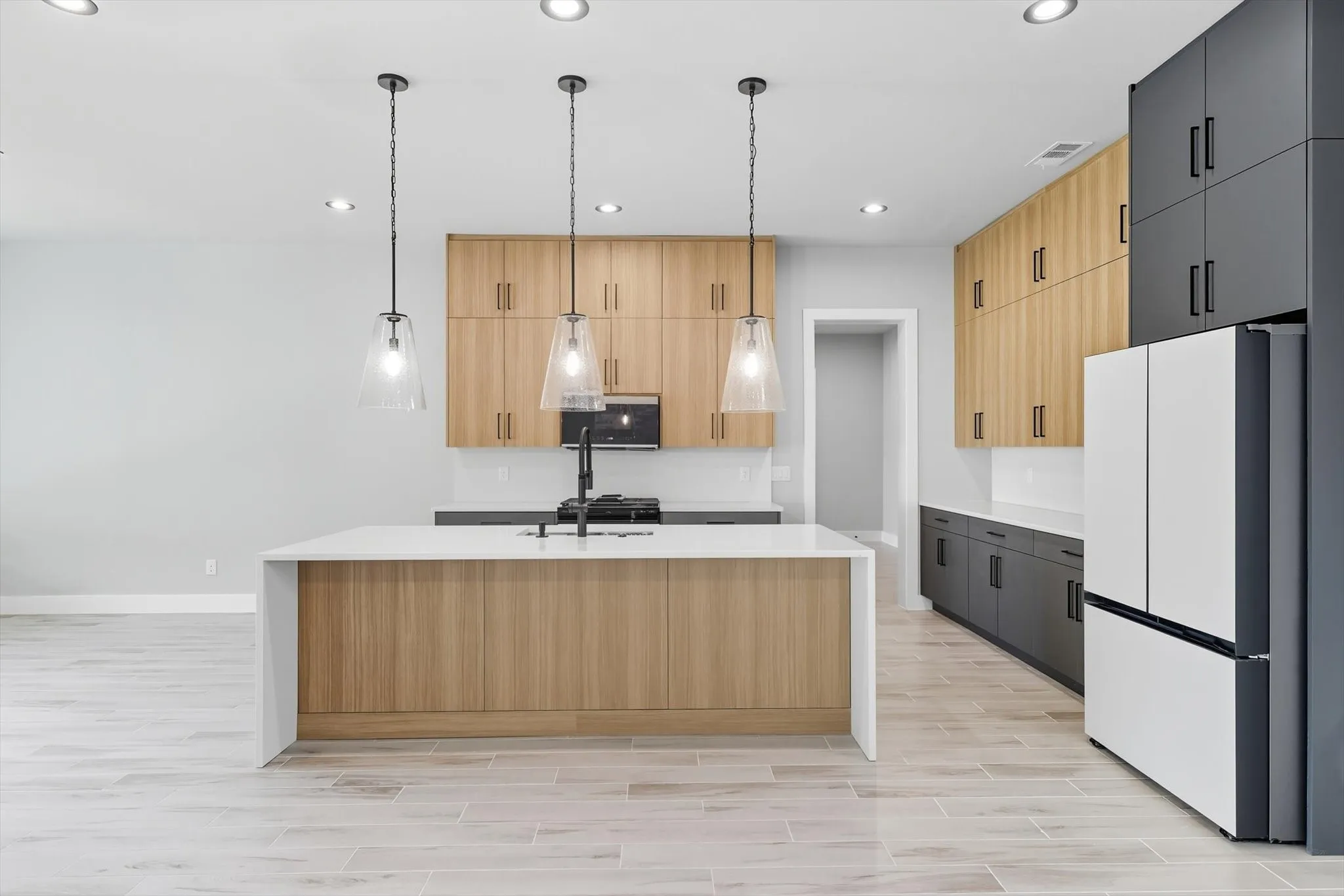 Kitchen with recessed lighting, freestanding refrigerator, wood tiled floors, light stone counters, and hanging light fixtures