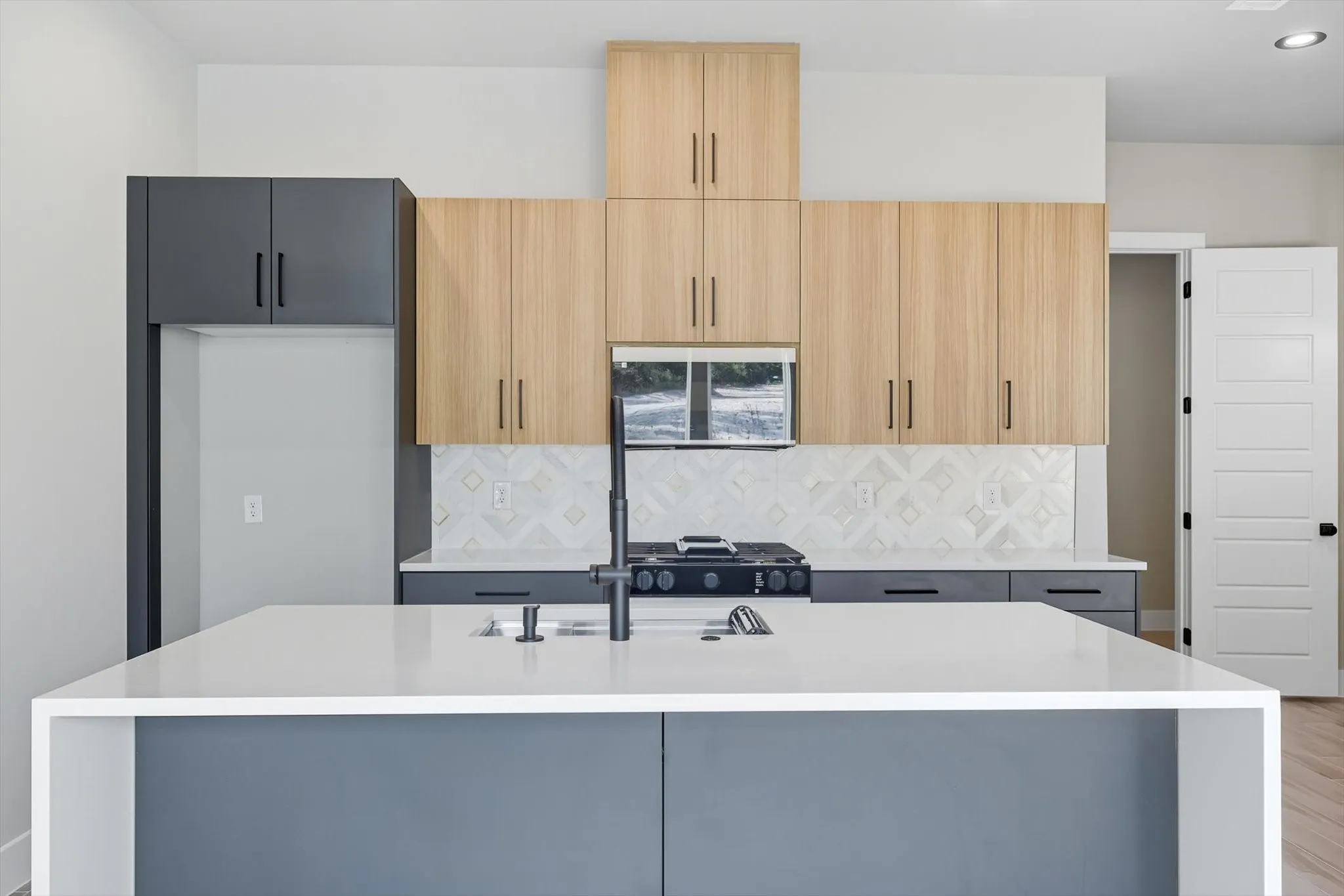 Kitchen with light stone counters, an island with sink, backsplash, modern cabinets, and light brown cabinets