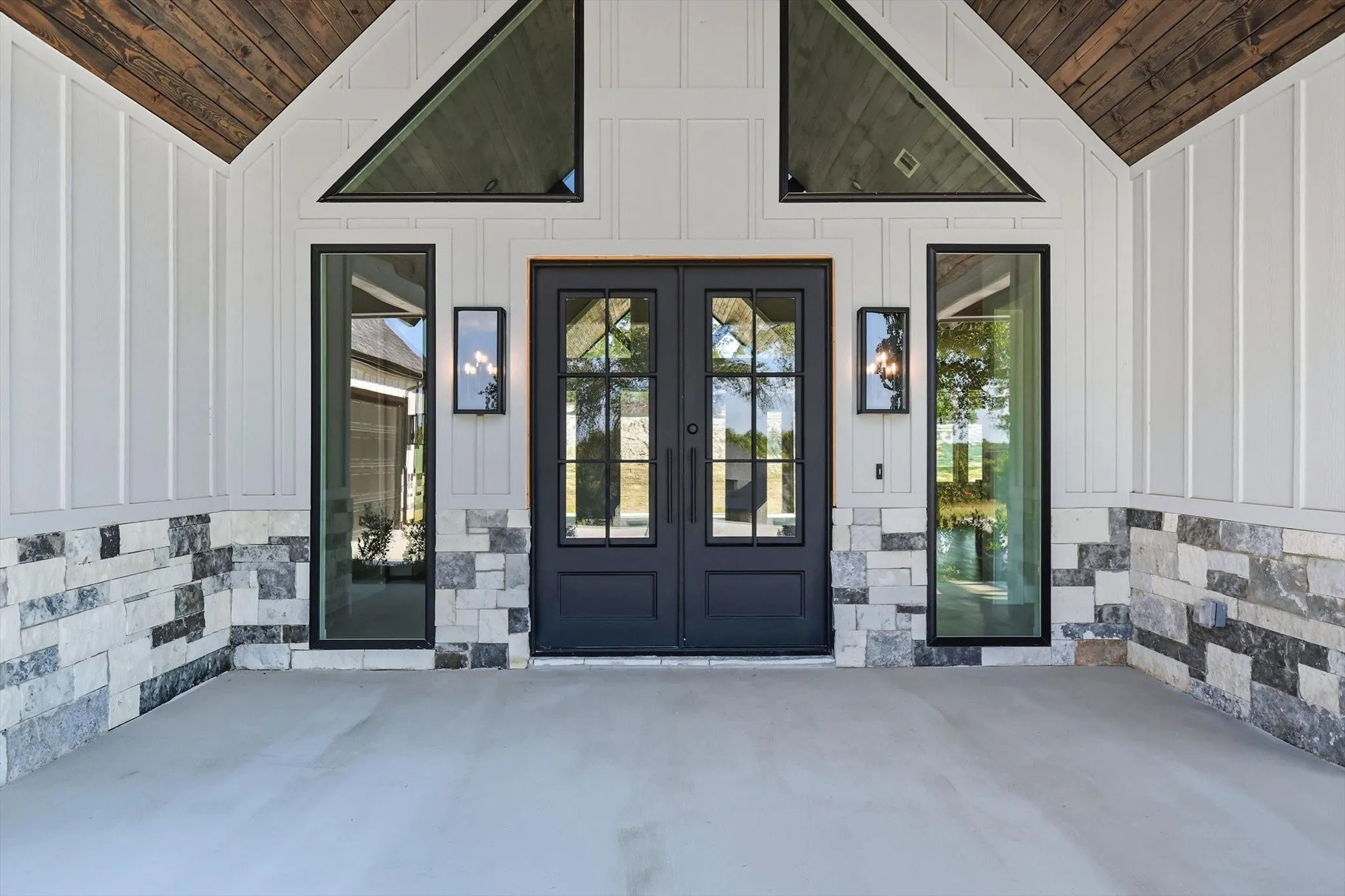 View of exterior entry with board and batten siding, a patio, and stone siding