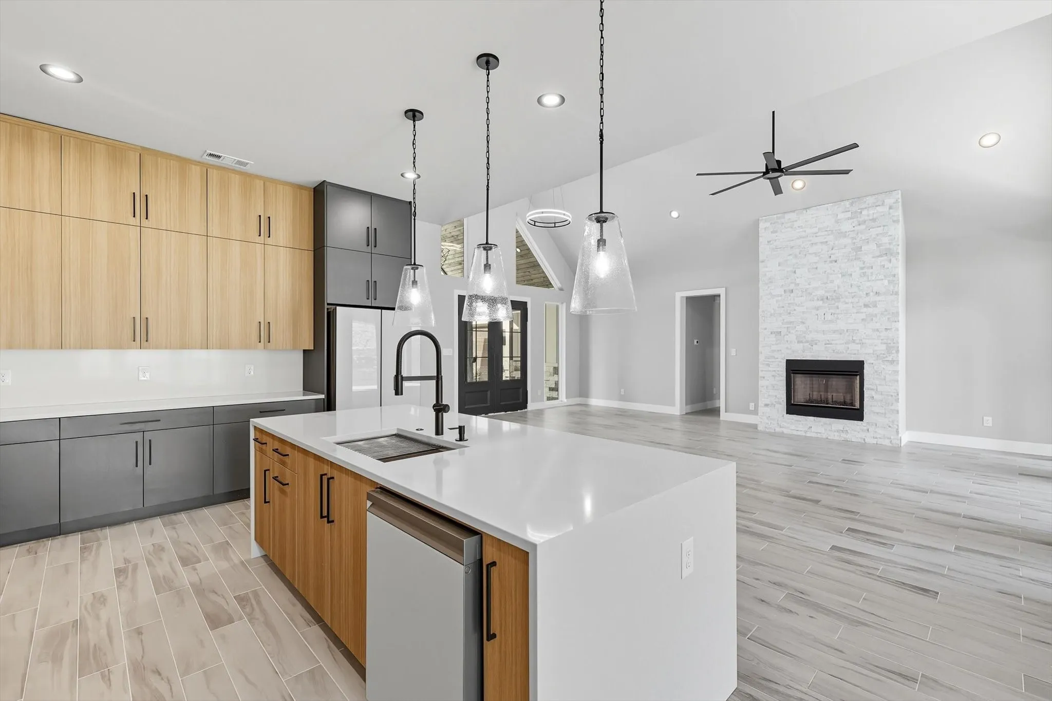 Kitchen with light brown cabinets, wood tiled floors, hanging light fixtures, light stone counters, and a kitchen island with sink