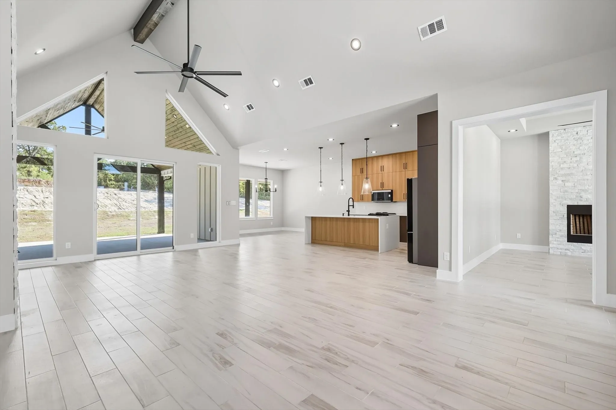 Unfurnished living room featuring high vaulted ceiling, beam ceiling, light wood-style floors, a fireplace, and ceiling fan
