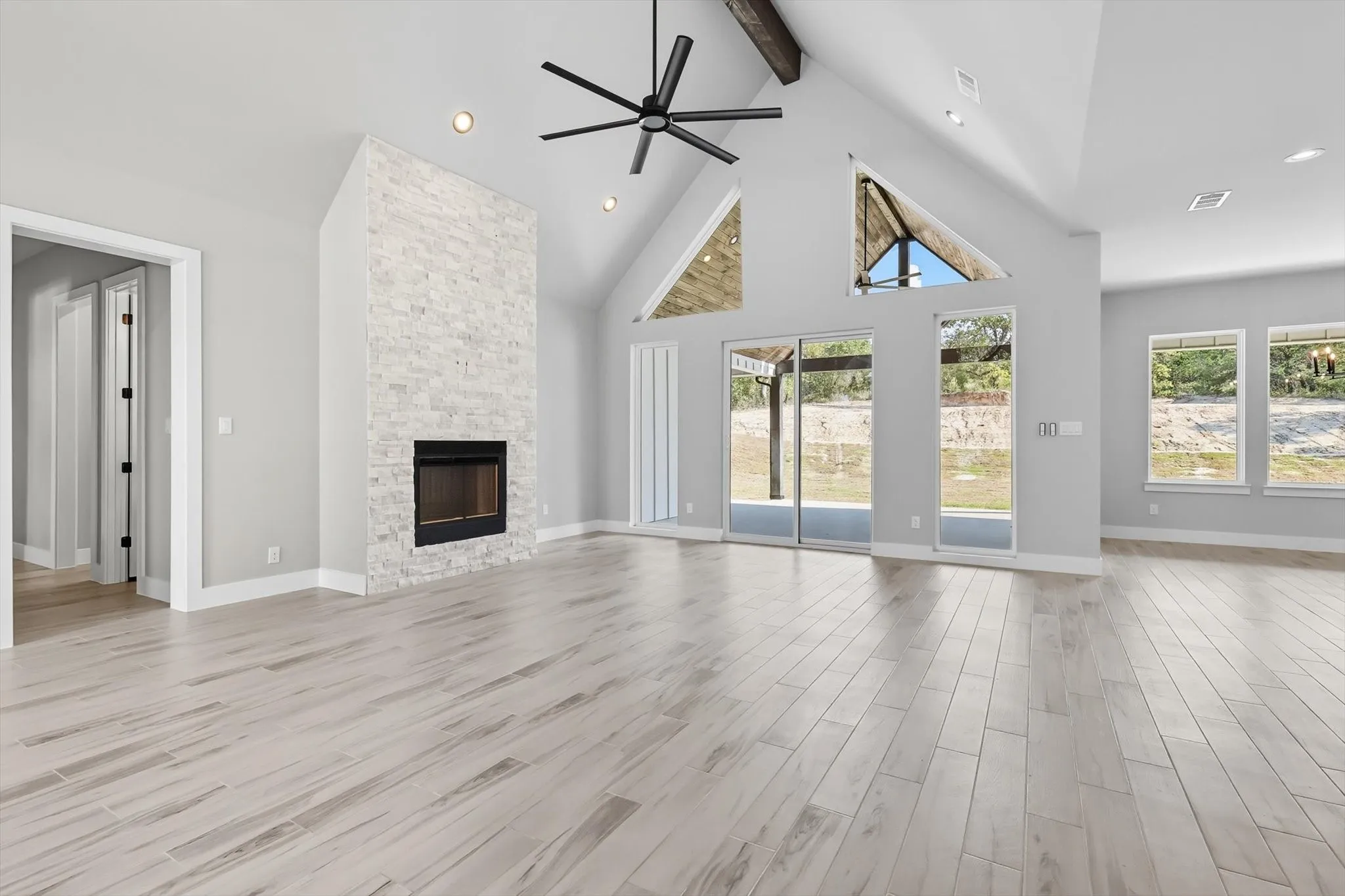 Unfurnished living room featuring beamed ceiling, high vaulted ceiling, a ceiling fan, light wood-type flooring, and a stone fireplace