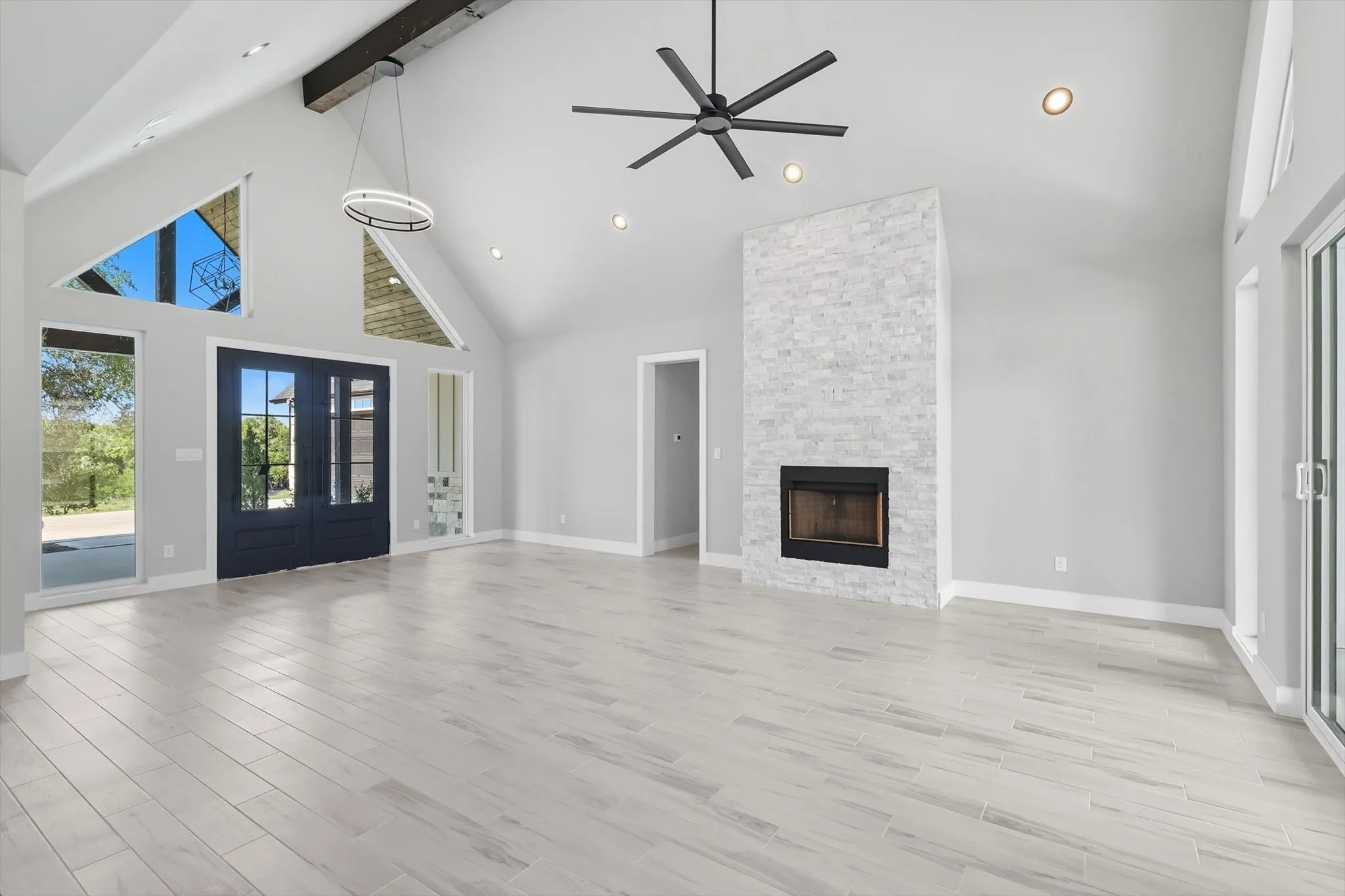 Unfurnished living room with high vaulted ceiling, french doors, beamed ceiling, light wood finished floors, and a stone fireplace