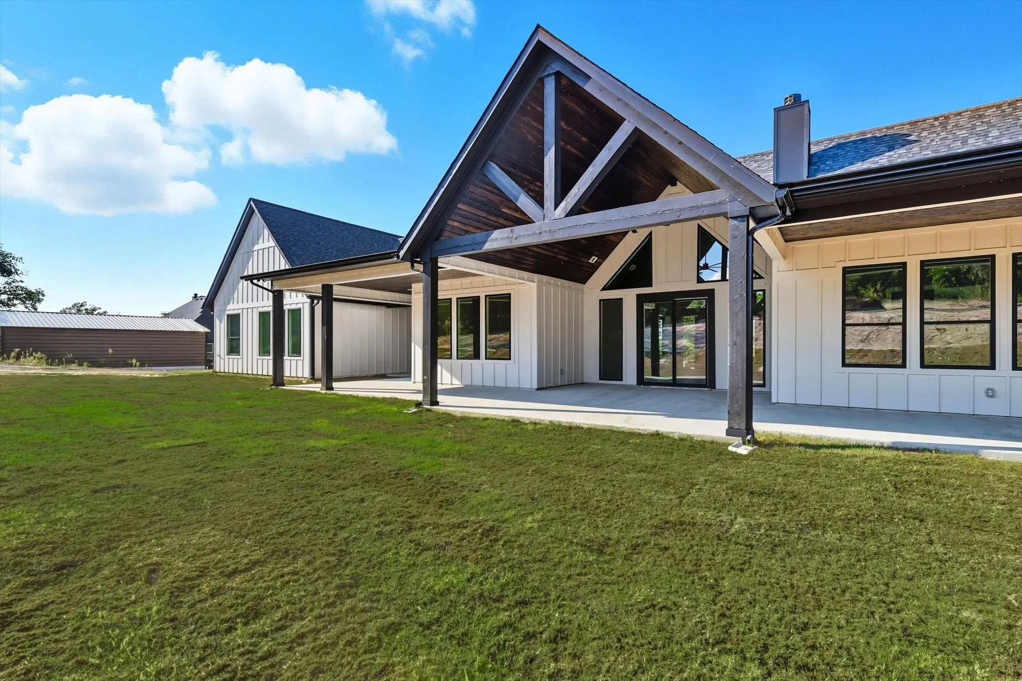 Back of house with board and batten siding, a patio area, a lawn, and a chimney