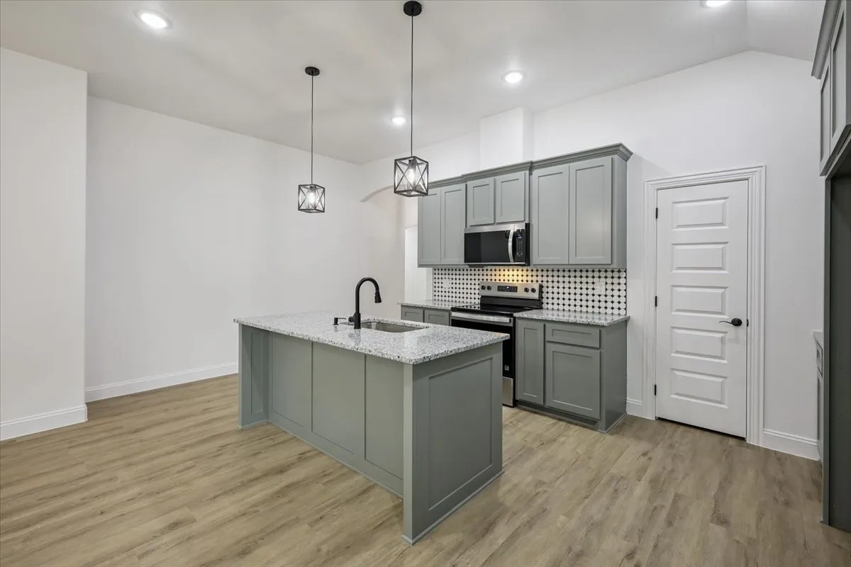Kitchen with stainless steel appliances, tasteful backsplash, gray cabinets, a center island with sink, and pendant lighting