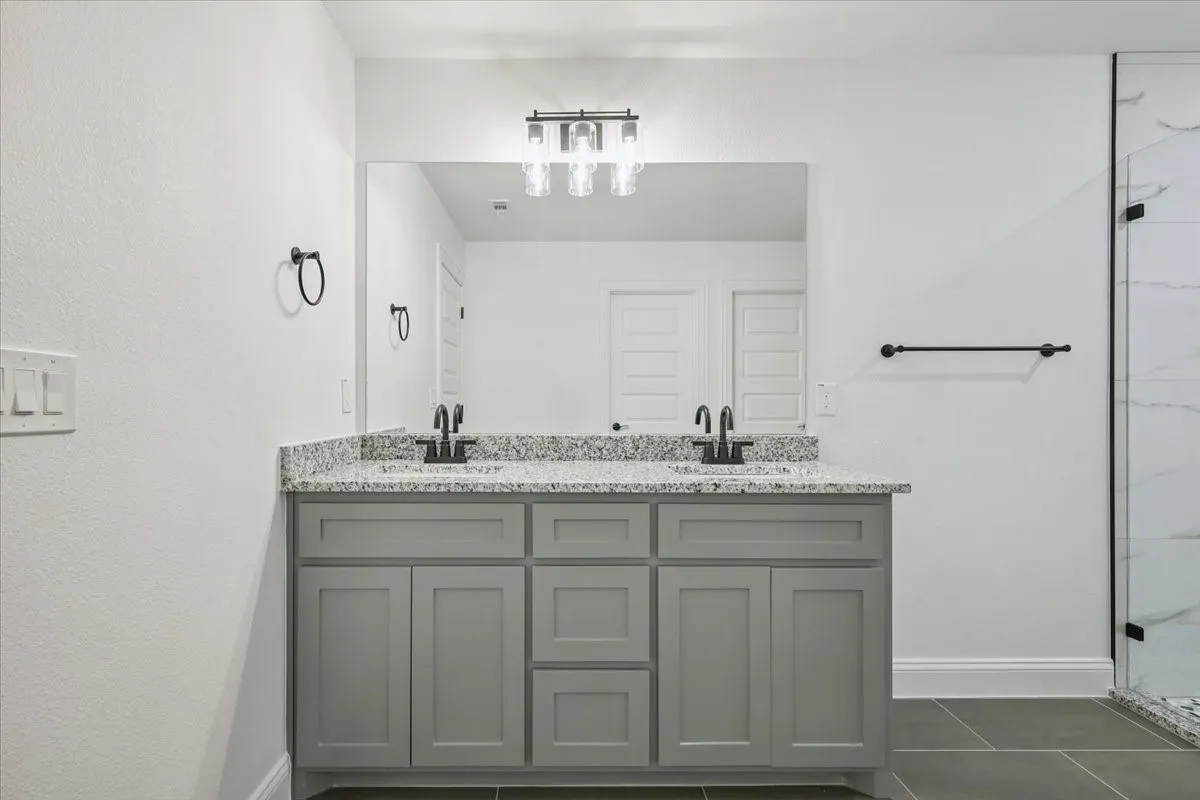 Full bath featuring double vanity, a marble finish shower, and dark tile patterned floors