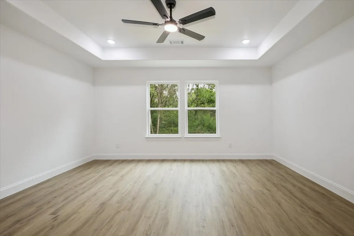Unfurnished room with light wood finished floors, a raised ceiling, ceiling fan, and recessed lighting