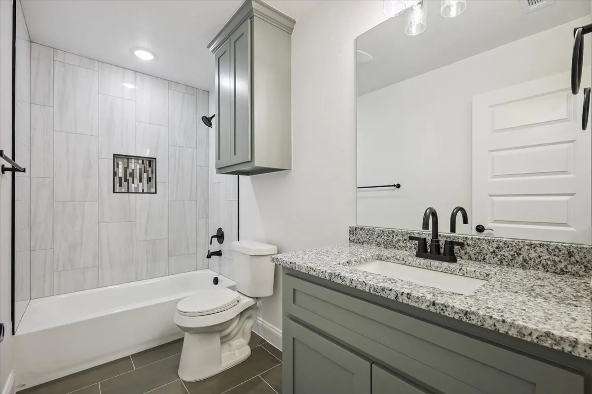 Full bath with washtub / shower combination, vanity, and dark tile patterned floors