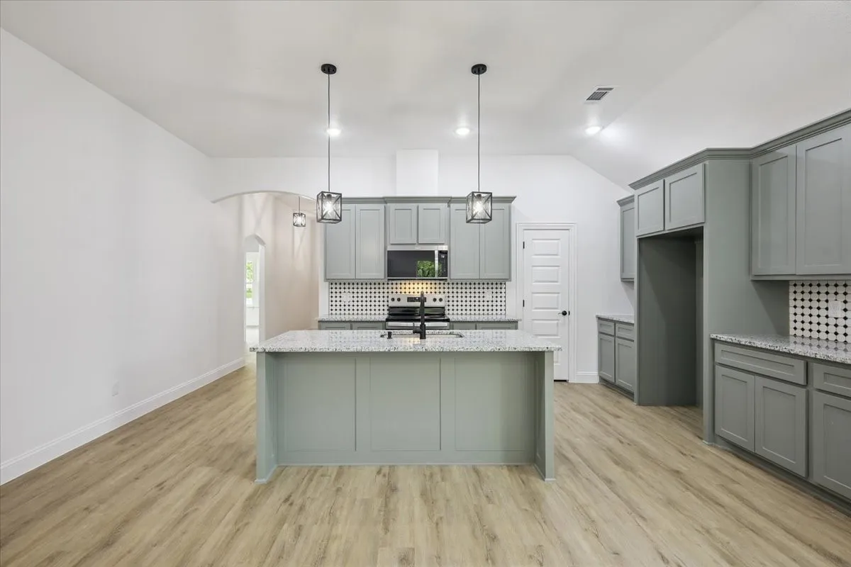 Kitchen with gray cabinetry, backsplash, arched walkways, light stone counters, and light wood-style flooring
