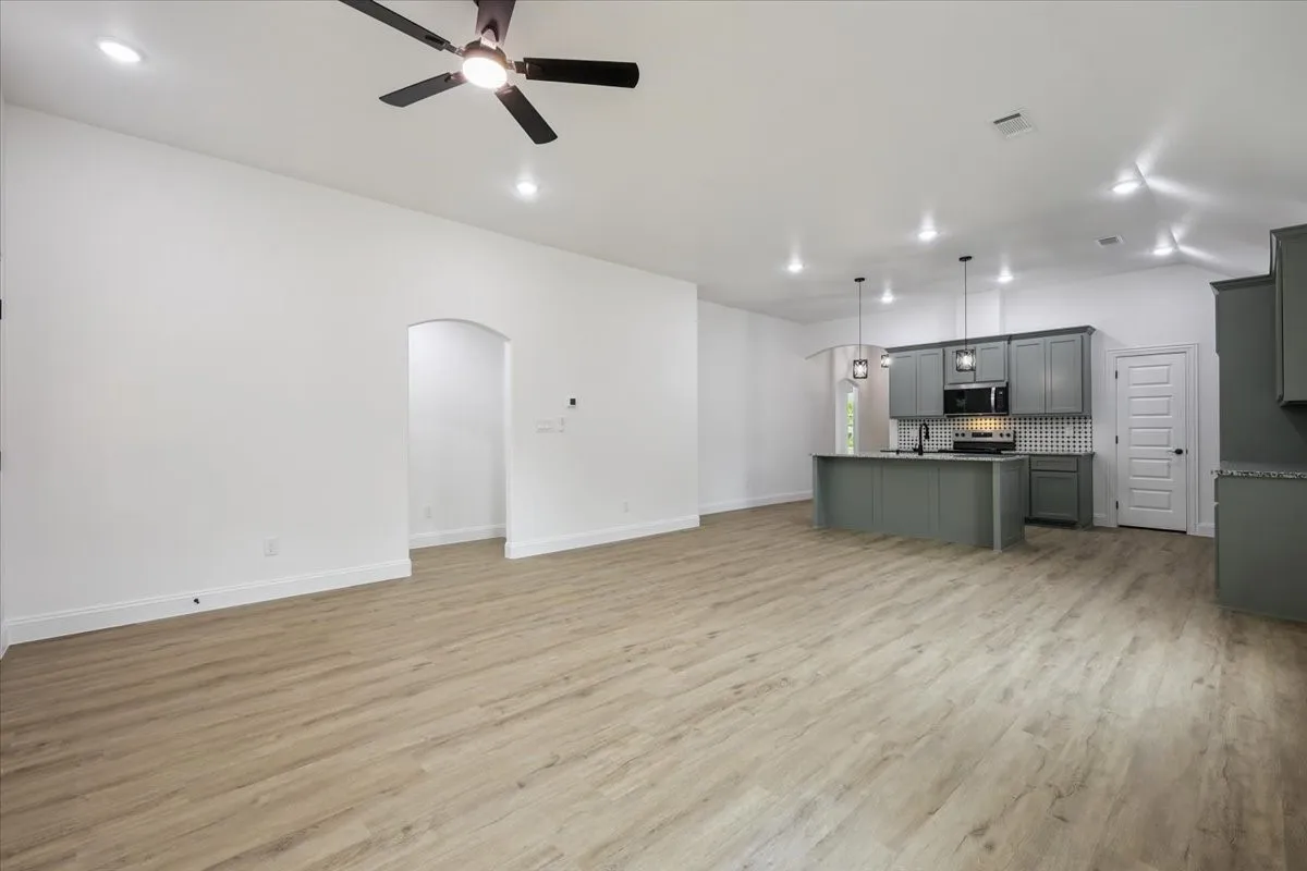Unfurnished living room with light wood-style flooring, arched walkways, ceiling fan, and recessed lighting