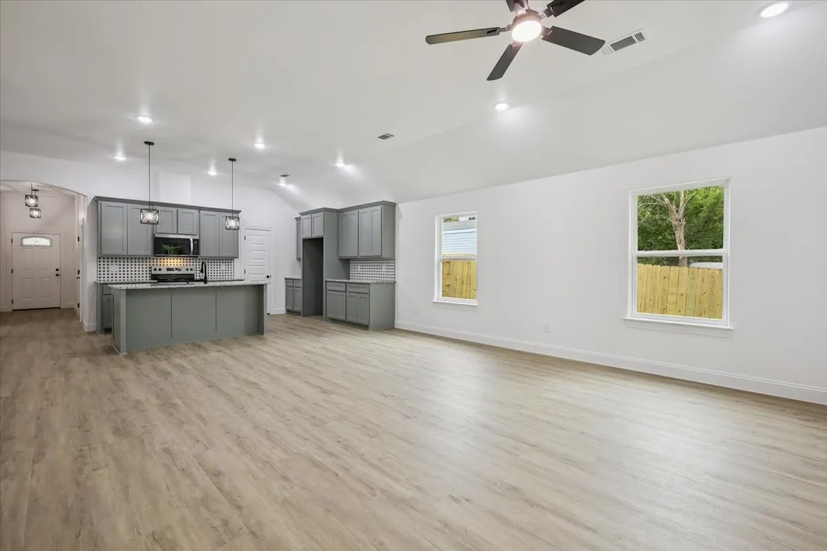 Unfurnished living room with lofted ceiling, light wood-type flooring, arched walkways, a ceiling fan, and recessed lighting