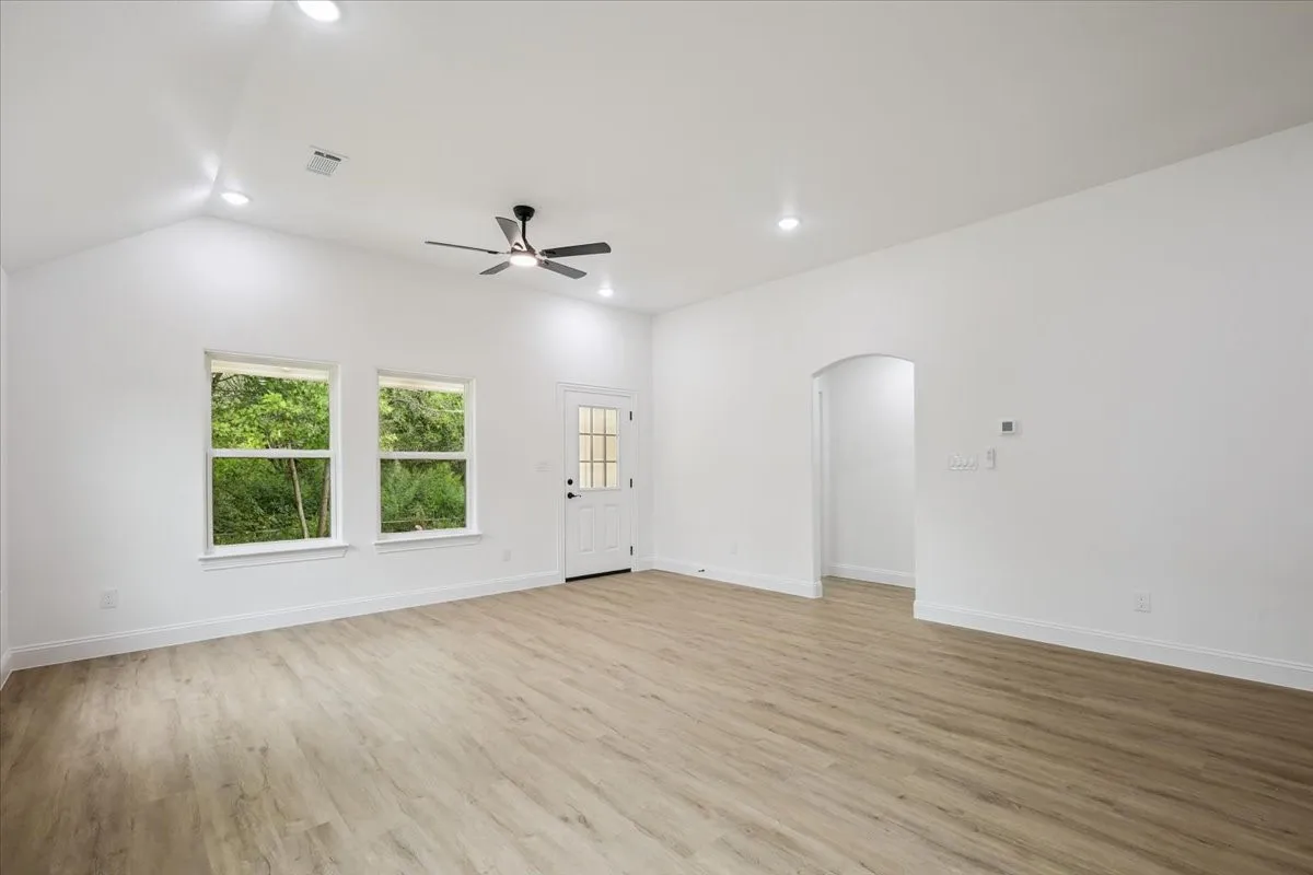 Unfurnished living room featuring light wood-style floors, arched walkways, recessed lighting, ceiling fan, and vaulted ceiling