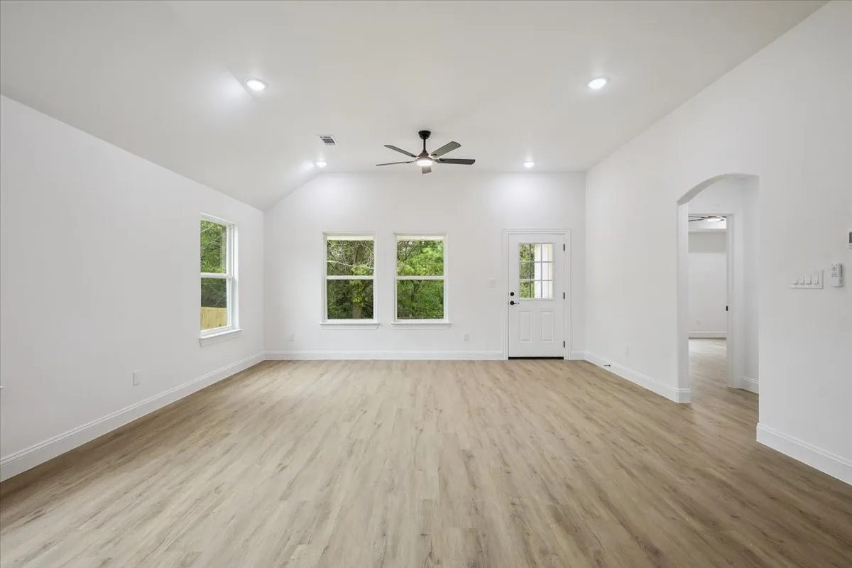 Unfurnished living room with arched walkways, light wood-style floors, recessed lighting, lofted ceiling, and a ceiling fan