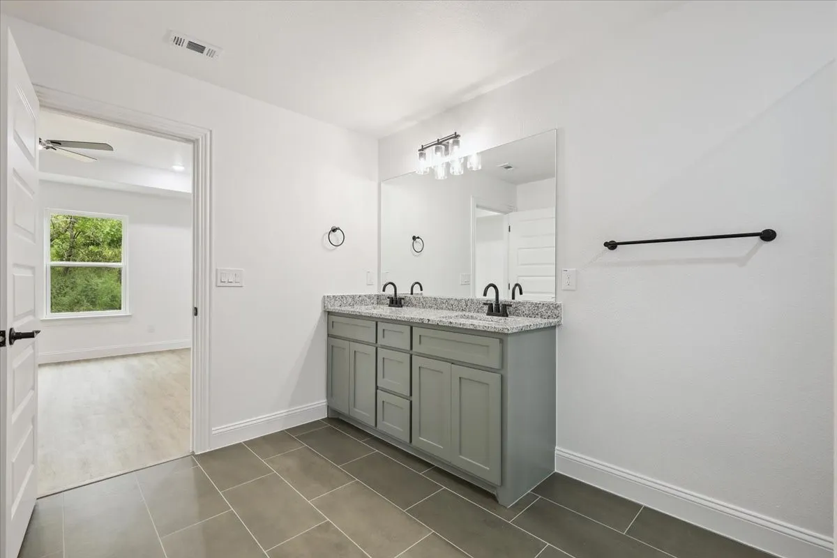 Bathroom with double vanity, dark tile patterned flooring, and a ceiling fan
