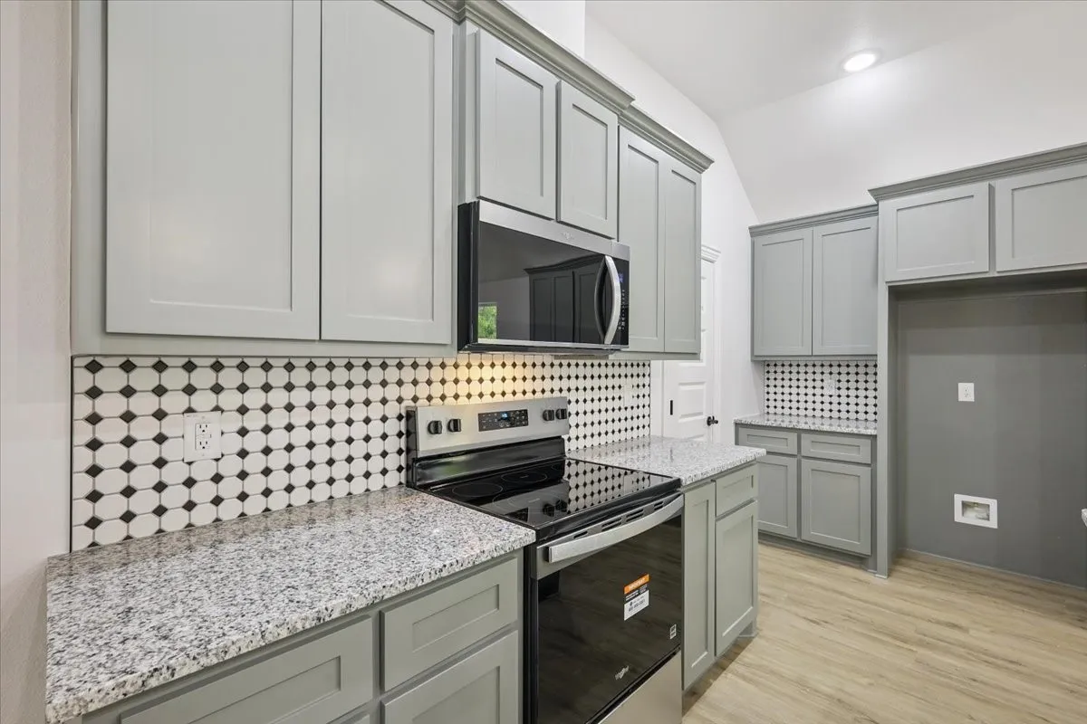 Kitchen featuring gray cabinets, appliances with stainless steel finishes, decorative backsplash, light stone counters, and vaulted ceiling