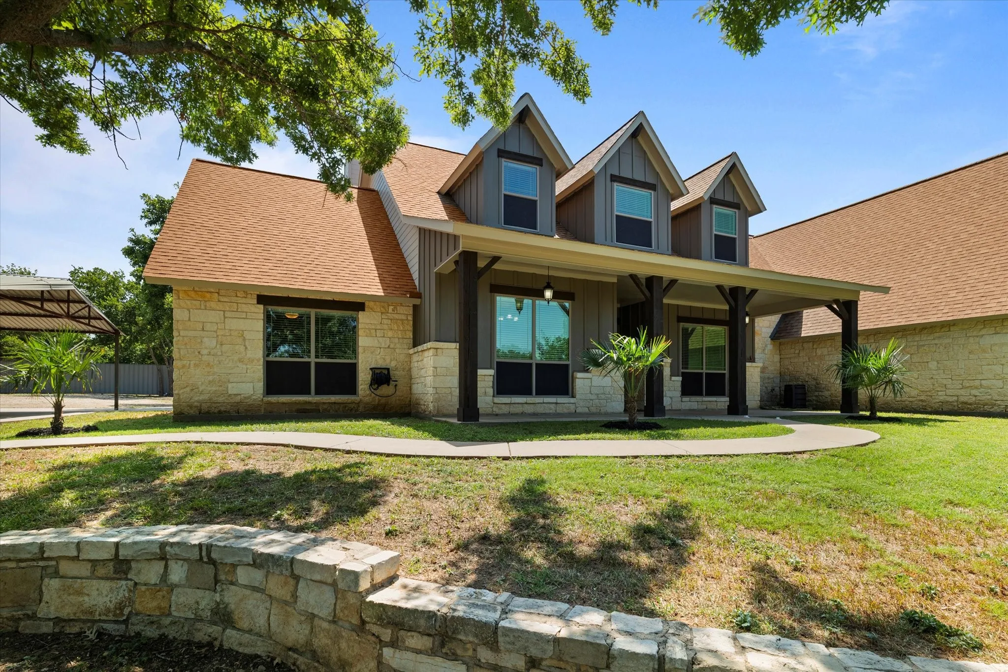 View of front of home with board and batten siding, stone siding, covered porch, and a shingled roof