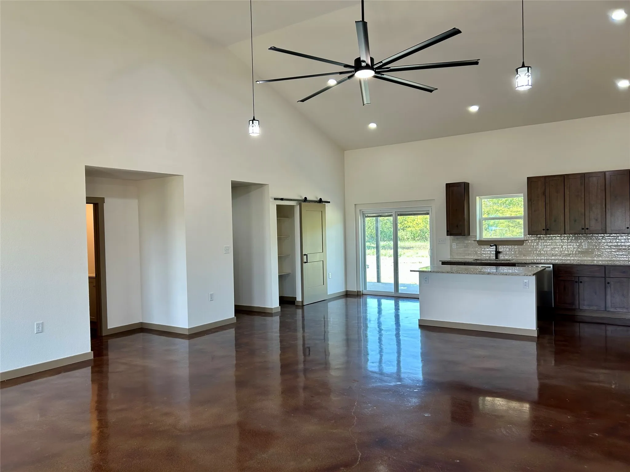 Kitchen with dark brown cabinetry, concrete floors, a barn door, decorative light fixtures, and high vaulted ceiling