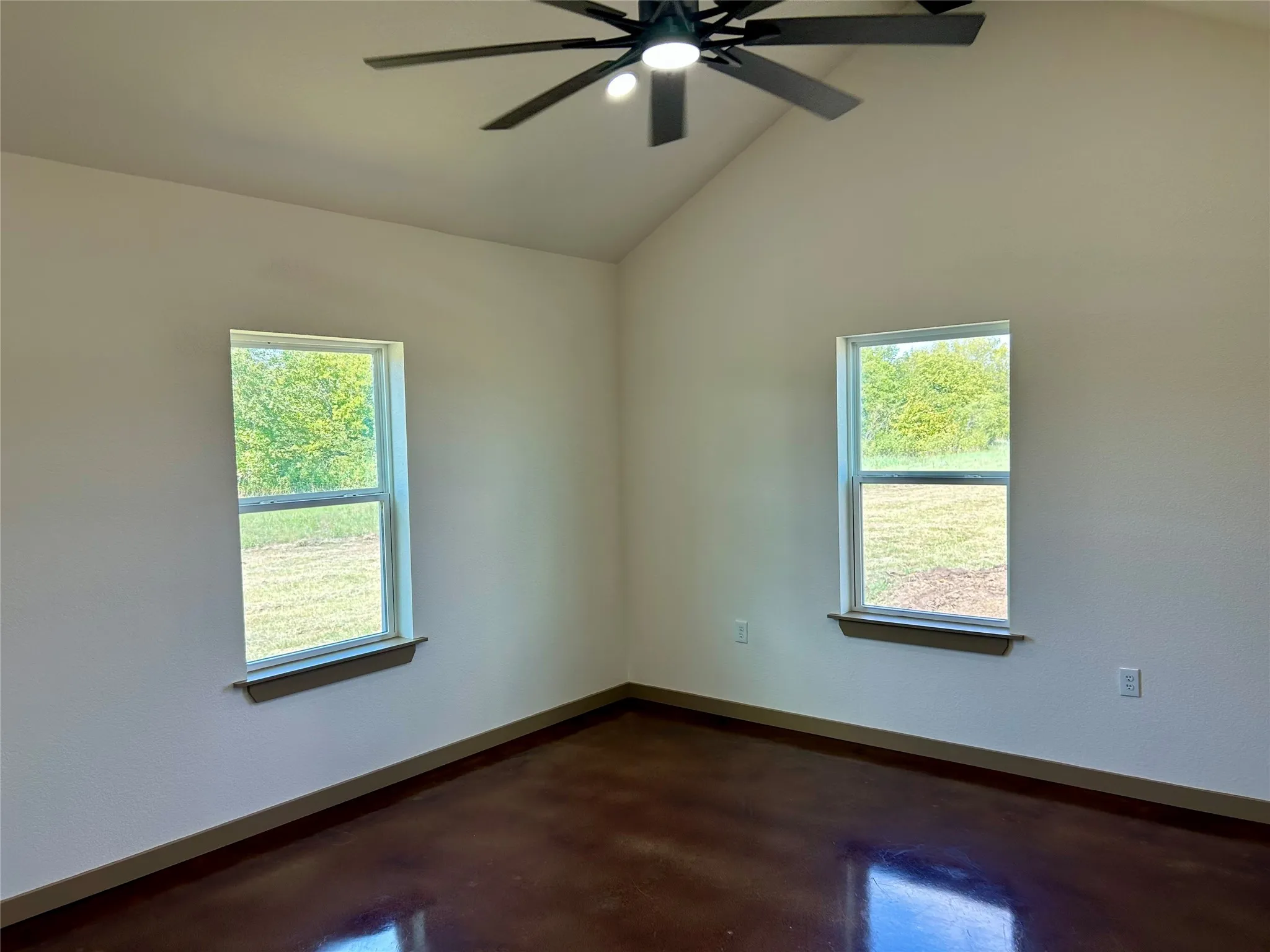 Empty room with finished concrete floors, lofted ceiling, and ceiling fan