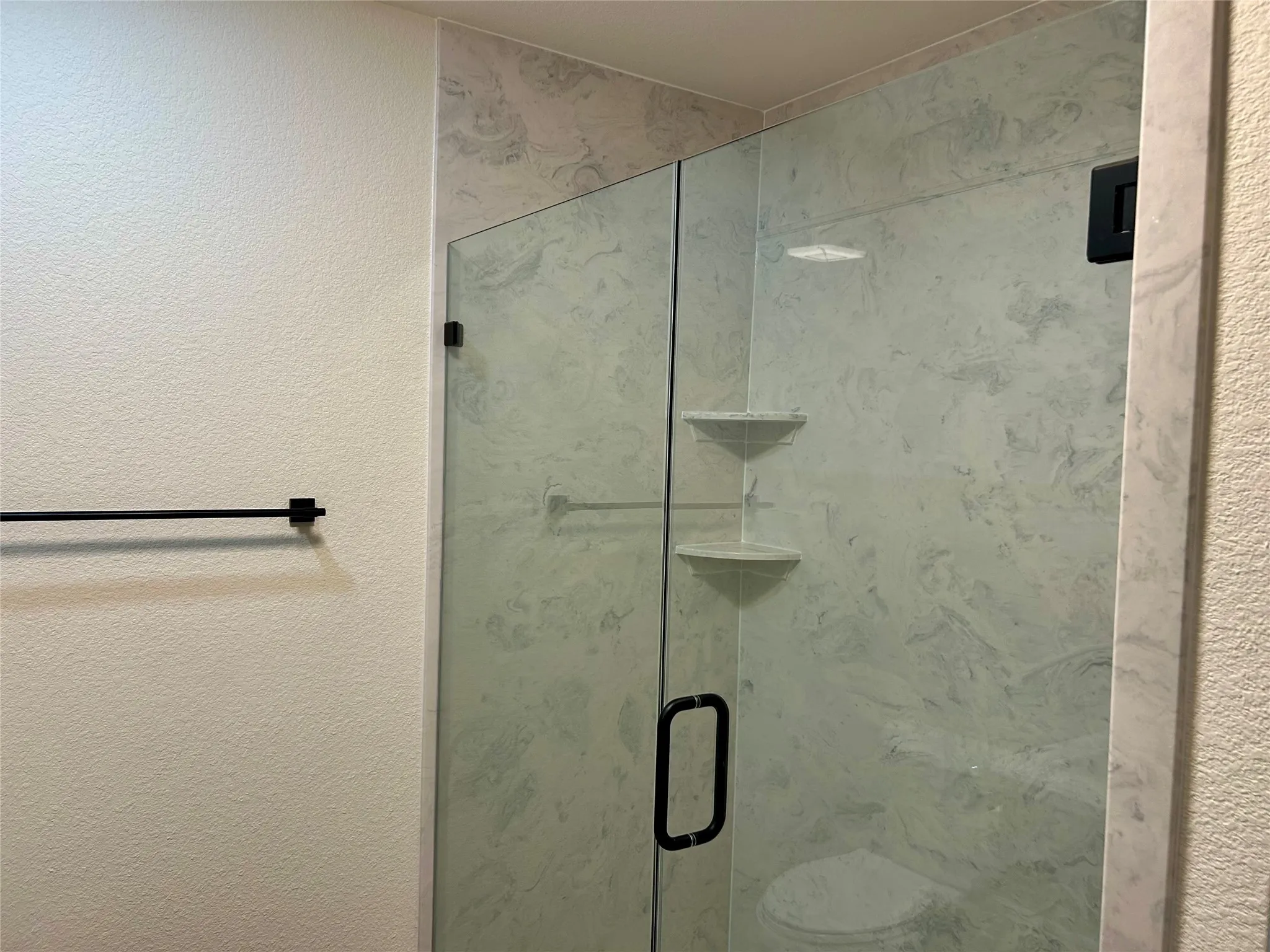 Full bathroom featuring a textured wall and a stall shower