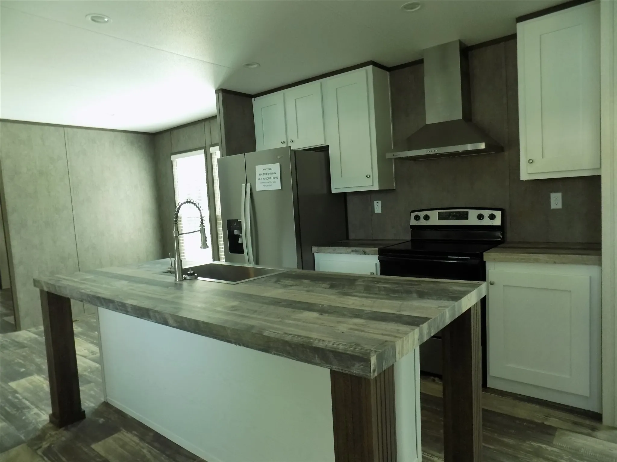 View of the great kitchen area with large kitchen isle and extraordinary faucet at large stainless steel sink. Dining area past refrigerator.