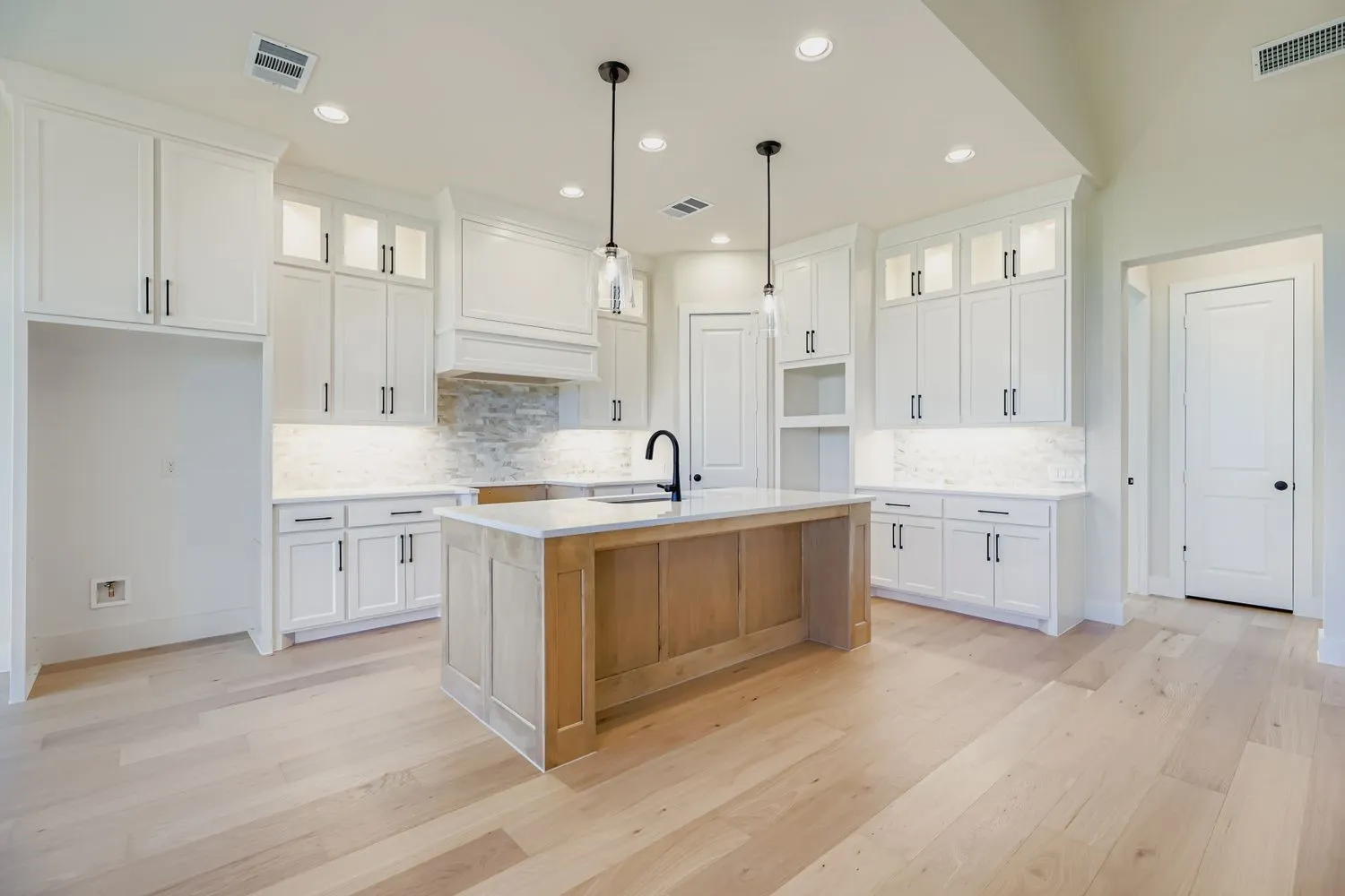 Kitchen with glass insert cabinets, white cabinetry, a kitchen island with sink, hanging light fixtures, and light wood-type flooring