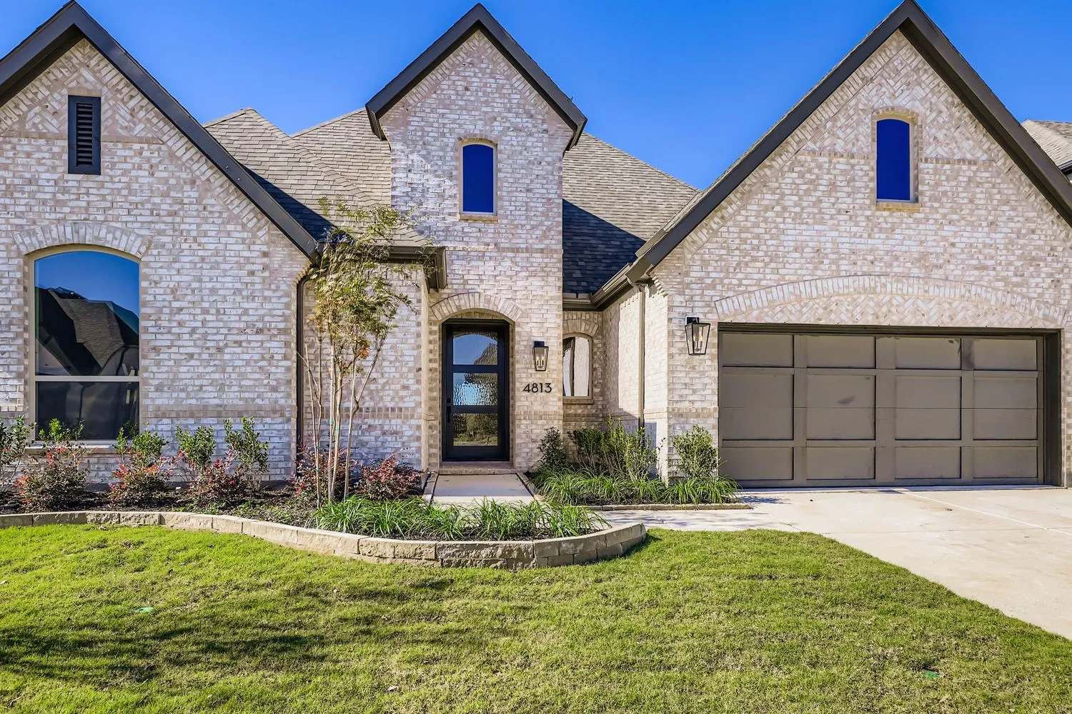 French country style house featuring brick siding, a front lawn, a shingled roof, driveway, and a garage