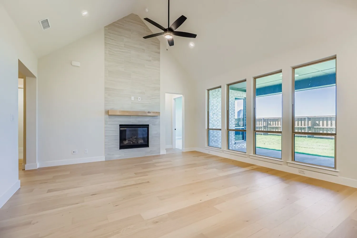 Unfurnished living room featuring high vaulted ceiling, light wood-style floors, a tiled fireplace, and a ceiling fan