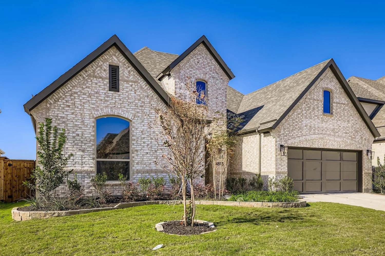 French country inspired facade featuring brick siding, a garage, driveway, and a shingled roof