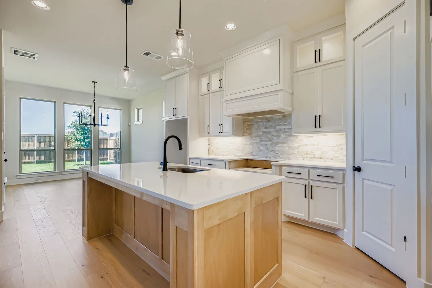 Kitchen with tasteful backsplash, white cabinetry, a center island with sink, light wood-style floors, and pendant lighting