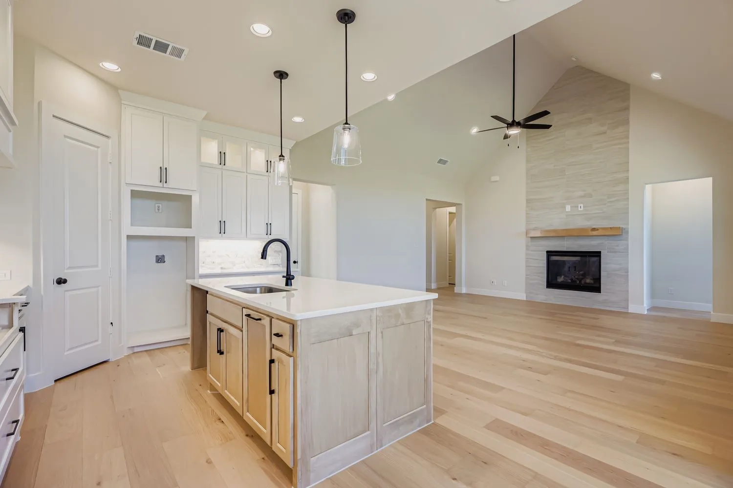 Kitchen with high vaulted ceiling, open floor plan, a kitchen island with sink, light wood finished floors, and pendant lighting