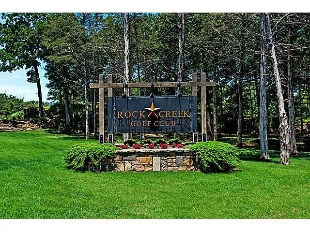 Community sign featuring a yard and view of wooded area