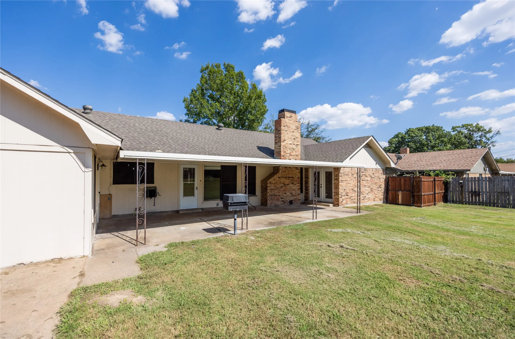 Rear view of property featuring a patio, roof with shingles, a chimney, and brick siding