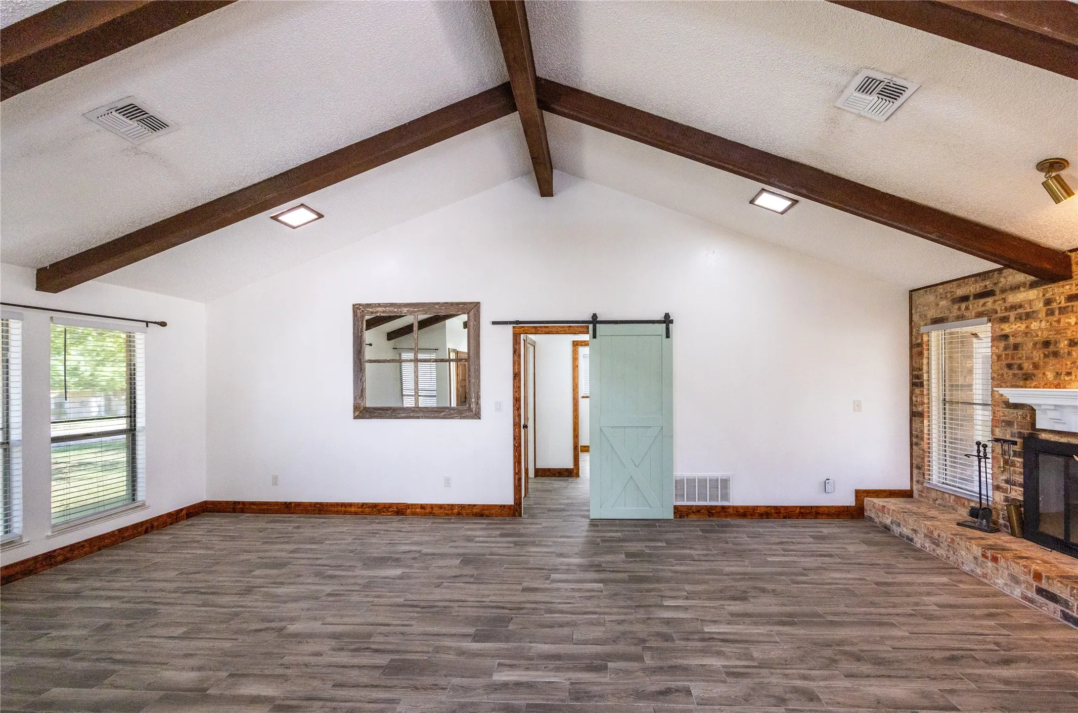 Unfurnished living room featuring beamed ceiling, a barn door, dark wood-style floors, a textured ceiling, and a glass covered fireplace