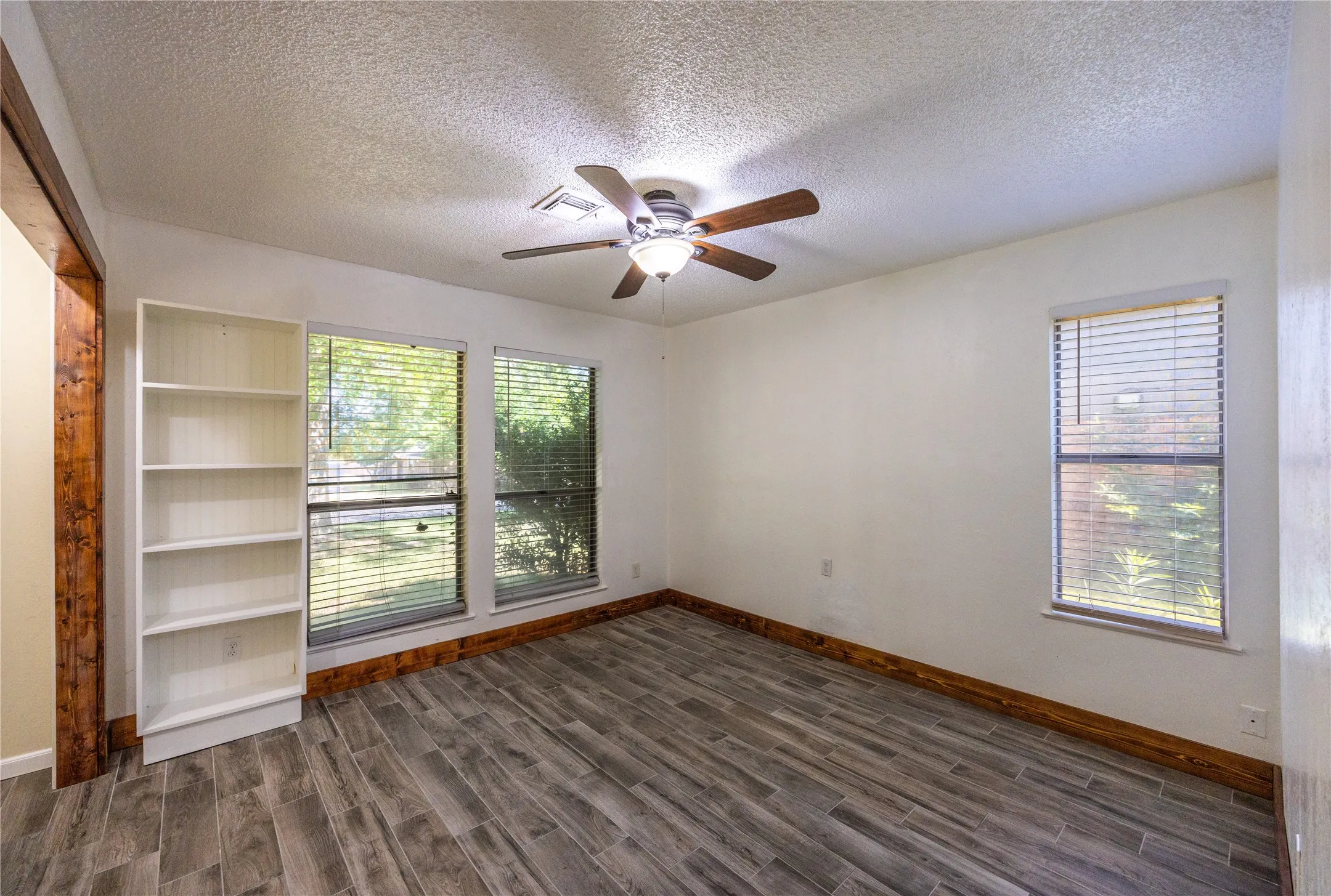 Empty room with dark wood-style floors, a textured ceiling, and ceiling fan