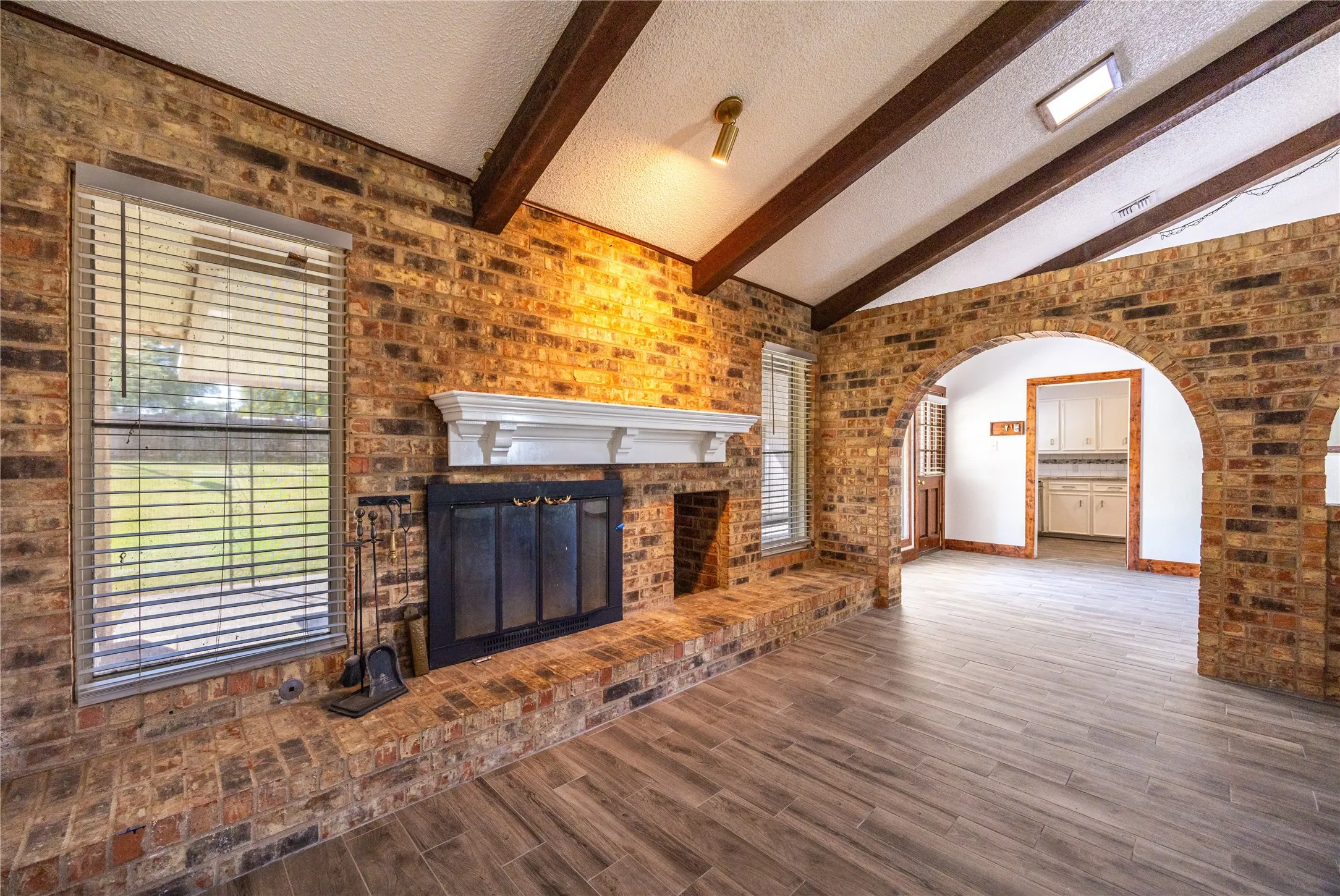Unfurnished living room featuring brick wall, a textured ceiling, a brick fireplace, wood finished floors, and arched walkways