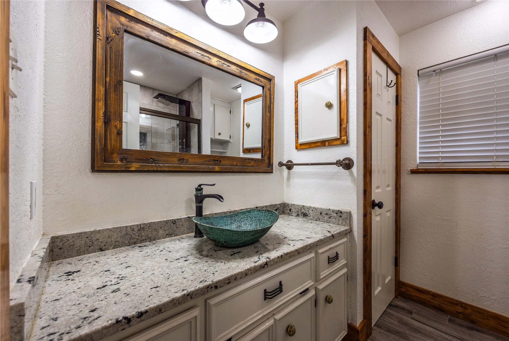 Full bathroom with a textured wall, vanity, and dark wood-style floors