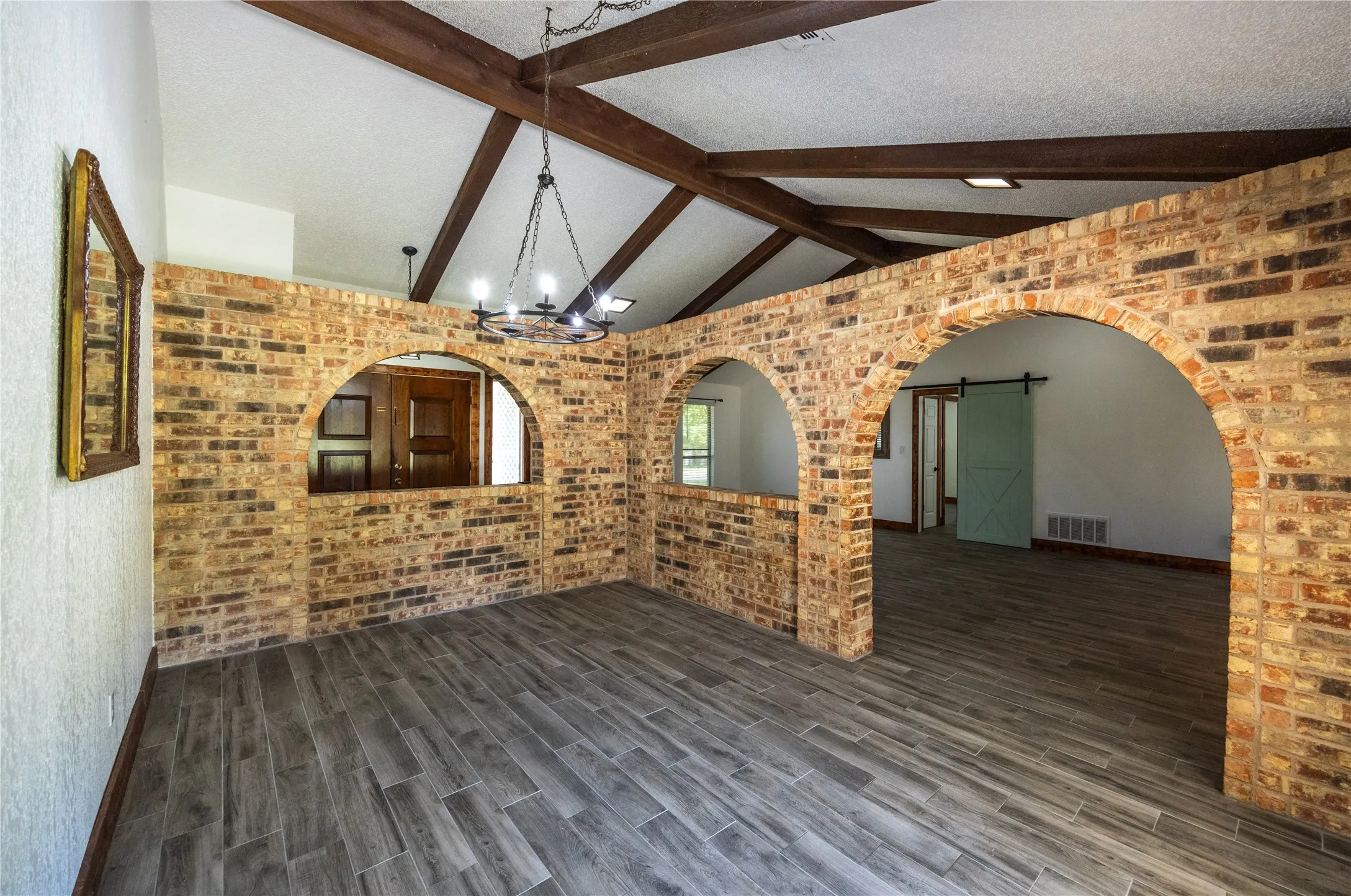 Empty room featuring brick wall, a barn door, a chandelier, arched walkways, and a textured ceiling