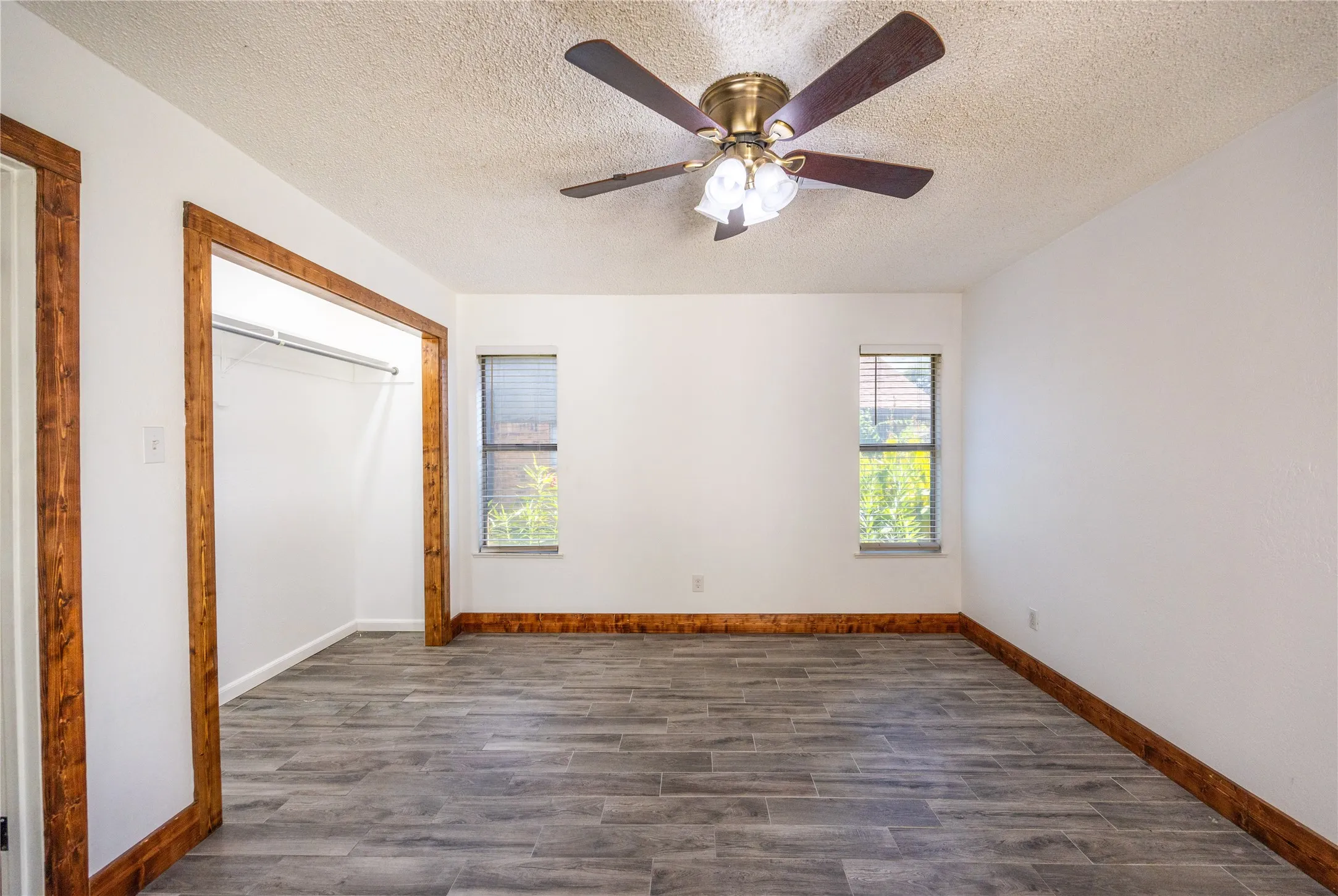 Unfurnished bedroom featuring a closet, a textured ceiling, wood finish floors, and ceiling fan