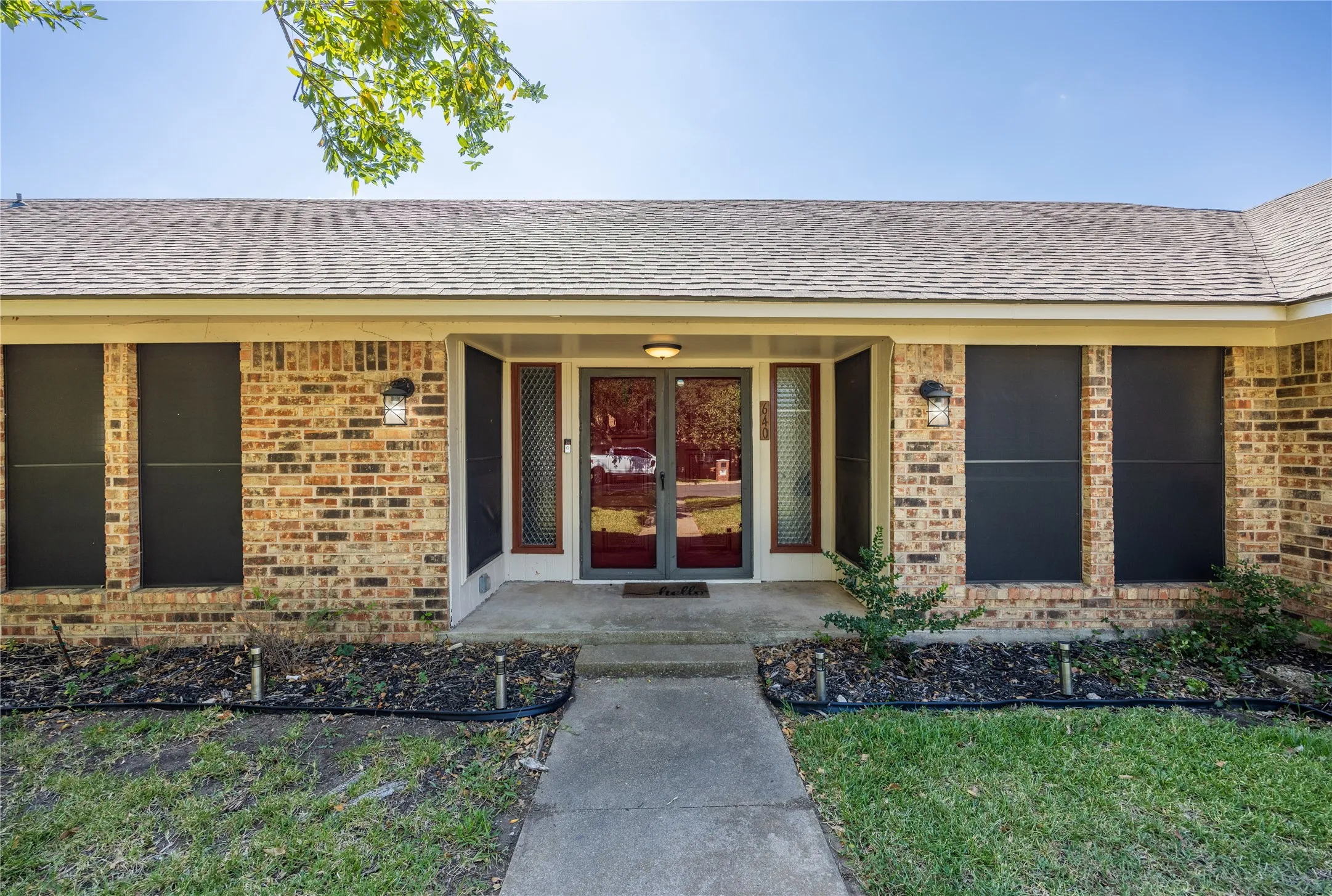 Entrance to property with brick siding, roof with shingles, and covered porch