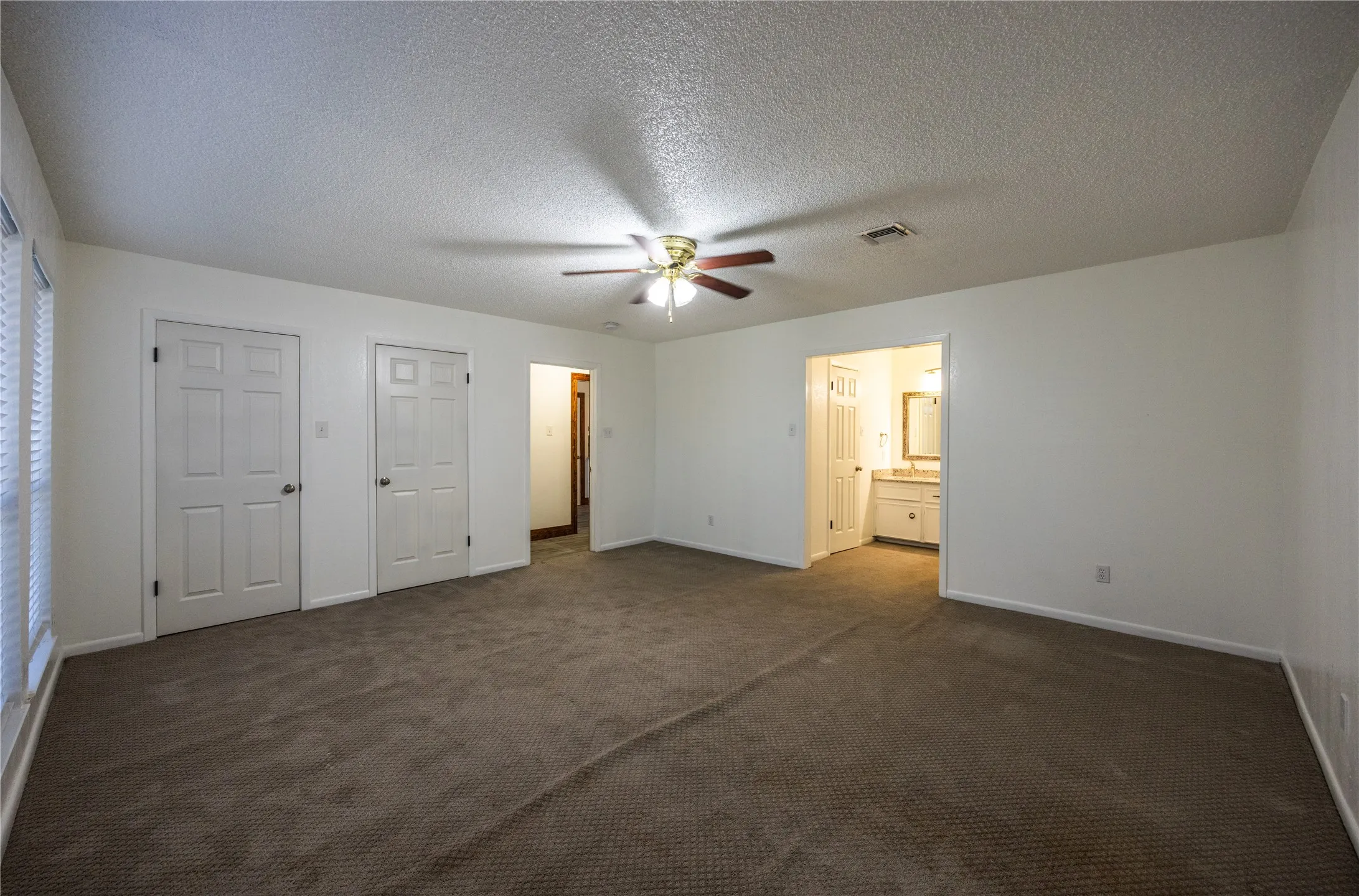 Unfurnished bedroom featuring dark carpet, a textured ceiling, ceiling fan, and ensuite bath