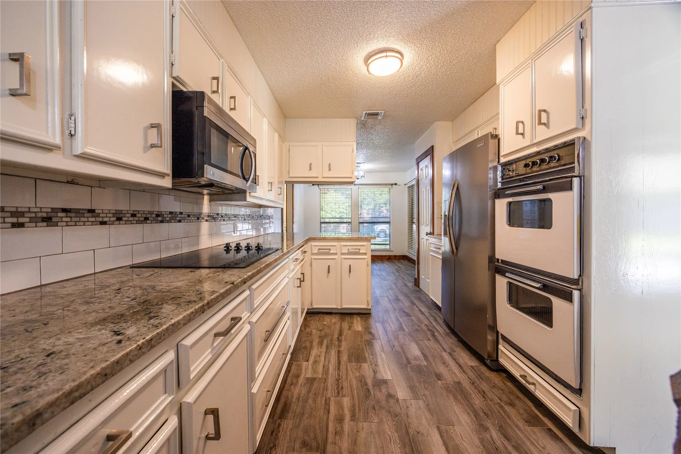 Kitchen featuring a textured ceiling, a peninsula, stainless steel appliances, dark wood finished floors, and tasteful backsplash