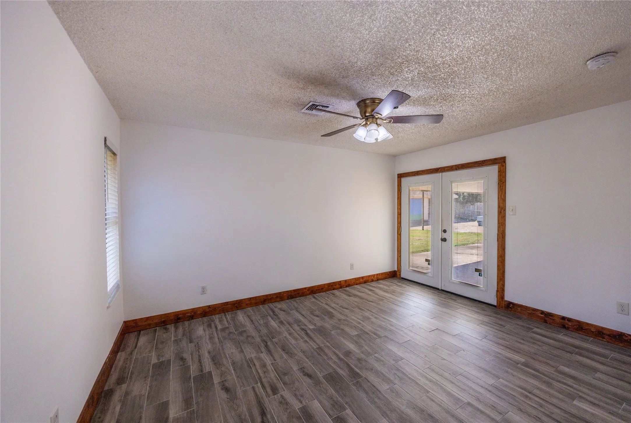 Unfurnished room with dark wood-style flooring, a textured ceiling, ceiling fan, and french doors