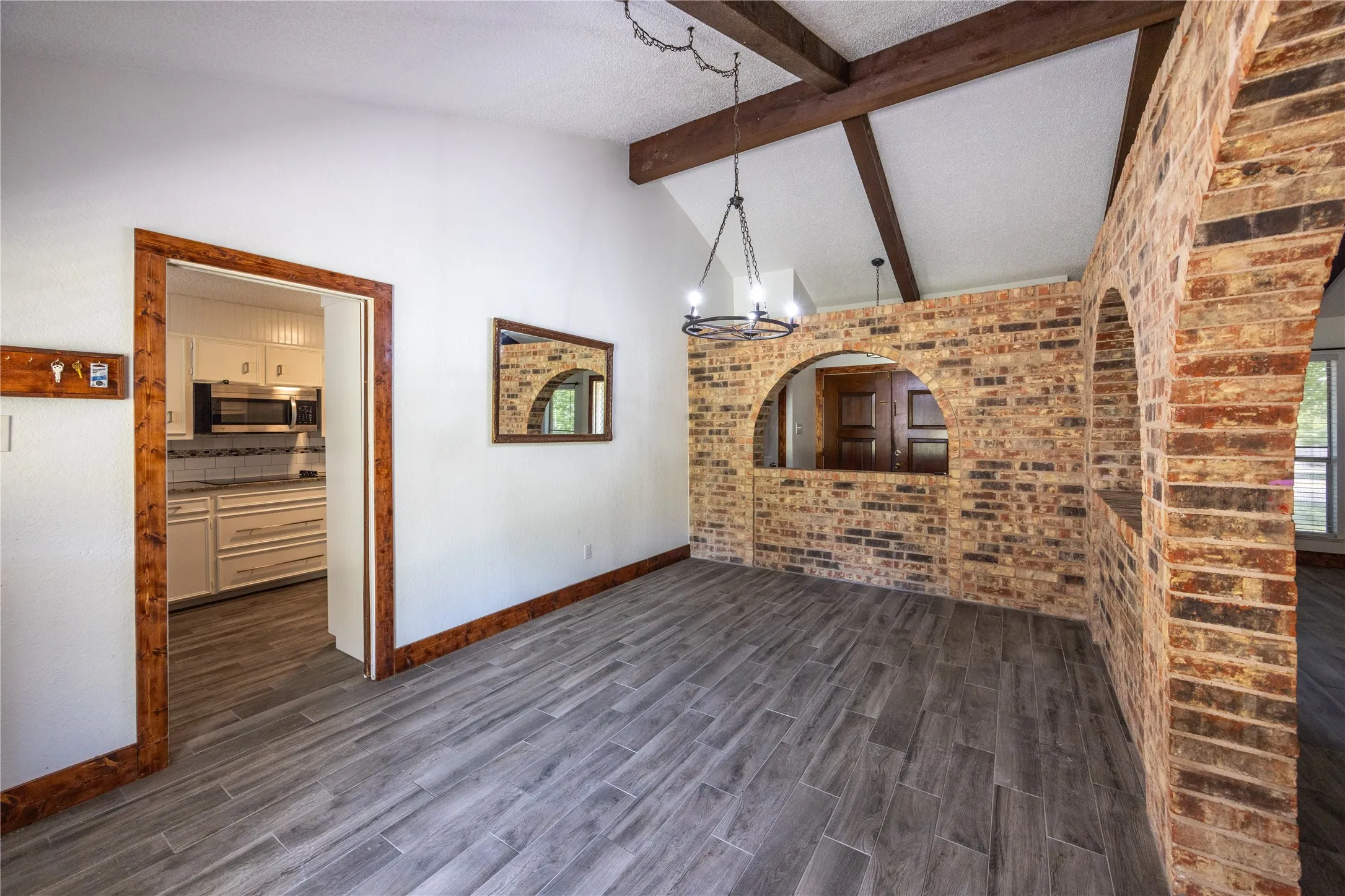 Unfurnished living room with brick wall, a chandelier, beam ceiling, dark wood-type flooring, and high vaulted ceiling