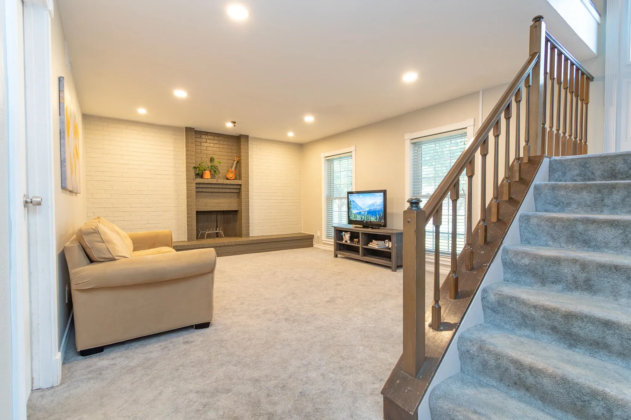 Living room featuring stairs, light carpet, recessed lighting, and a brick fireplace