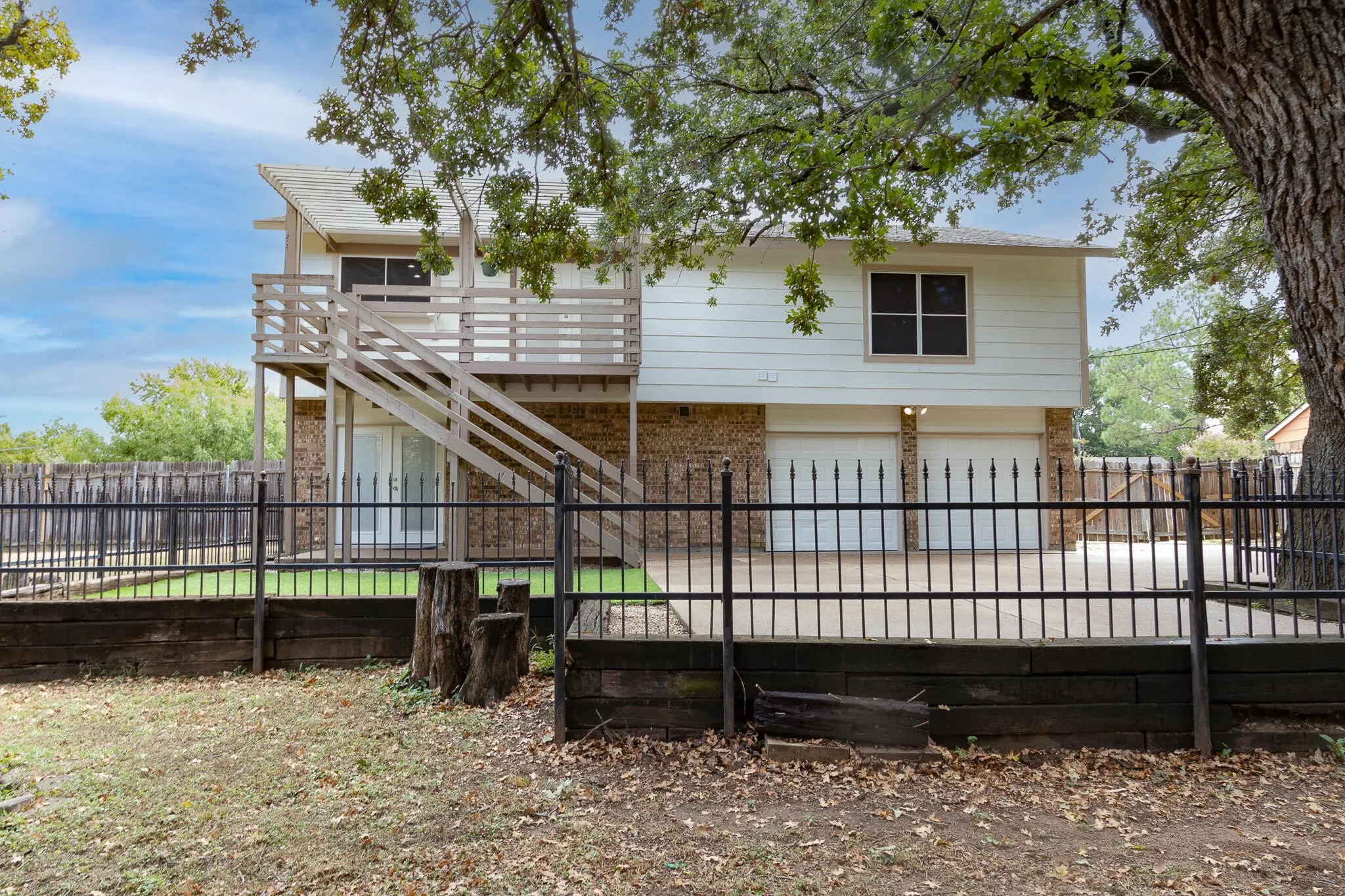 Rear view of property with brick siding, stairway, a fenced backyard, an attached garage, and a balcony